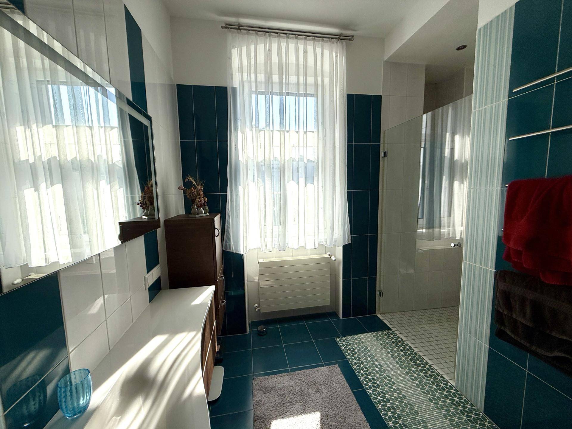 Modernes Badezimmer mit blauen und weißen Fliesen, großem Spiegel und Fenster, hell und freundlich.
