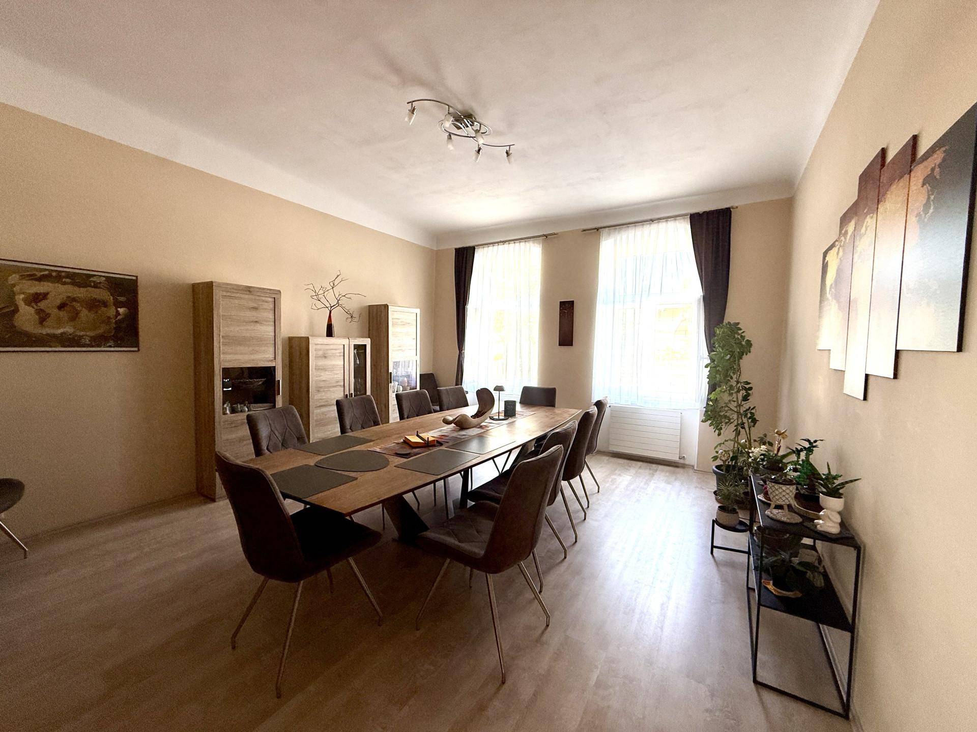 Geräumiges Esszimmer mit großem Holztisch, vielen Stühlen und hellem Laminatboden.