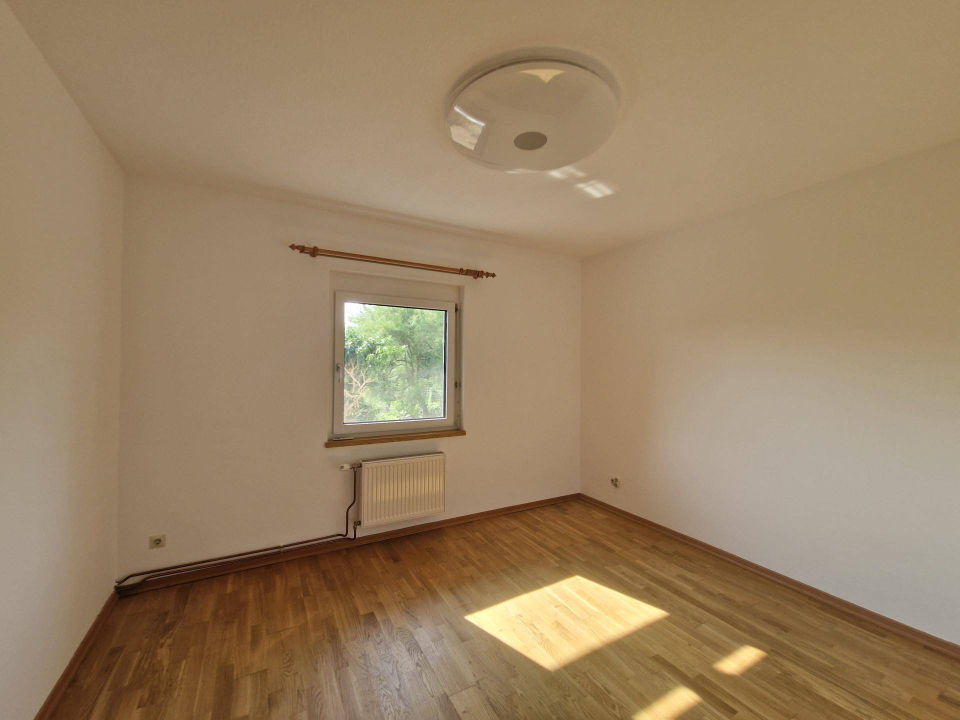 Geräumiges Schlafzimmer mit Holzboden, viel Tageslicht und Blick ins Grüne.