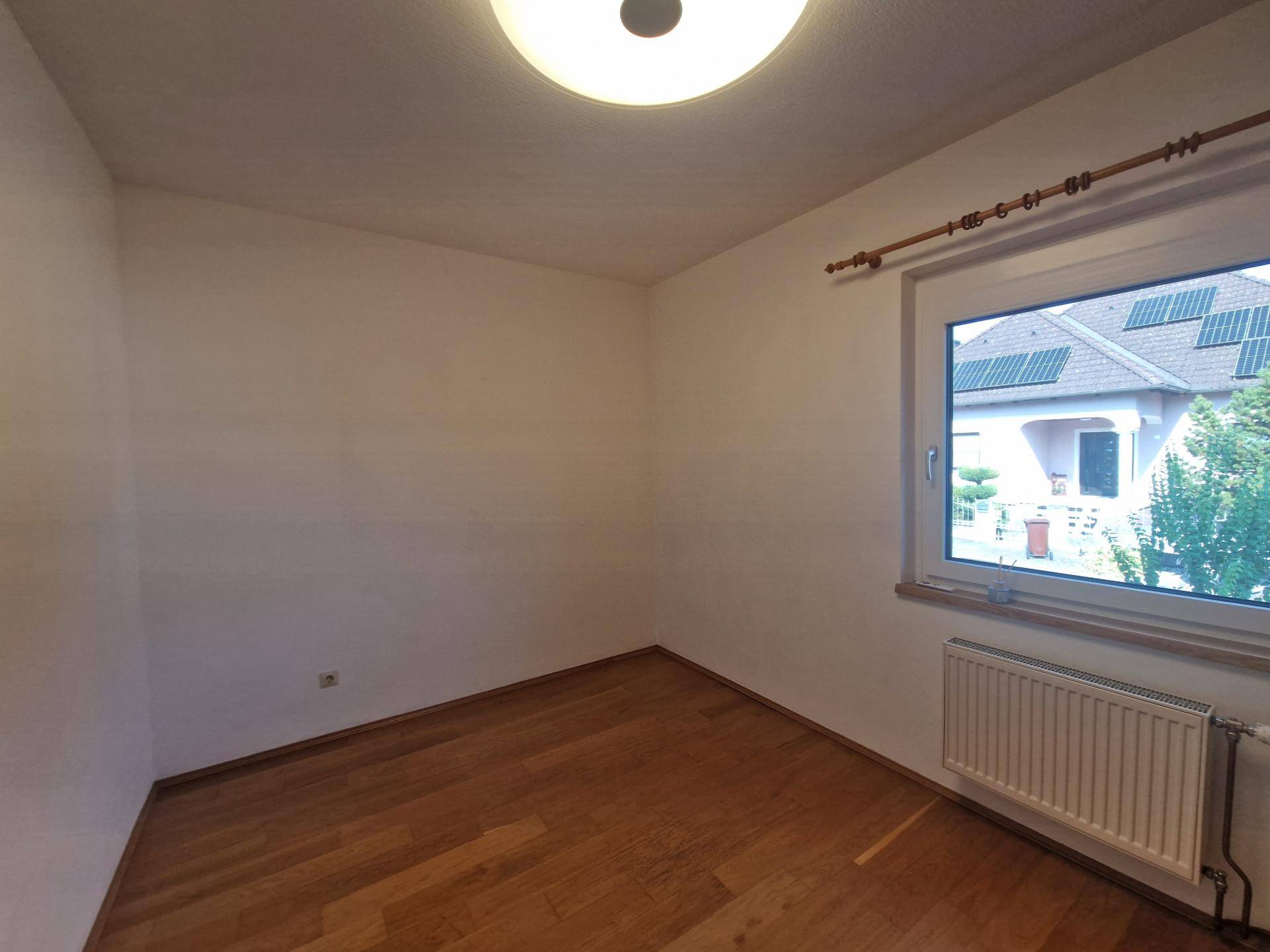 Helles Schlafzimmer mit Parkettboden, weiß gestrichenen Wänden und Fenster.
