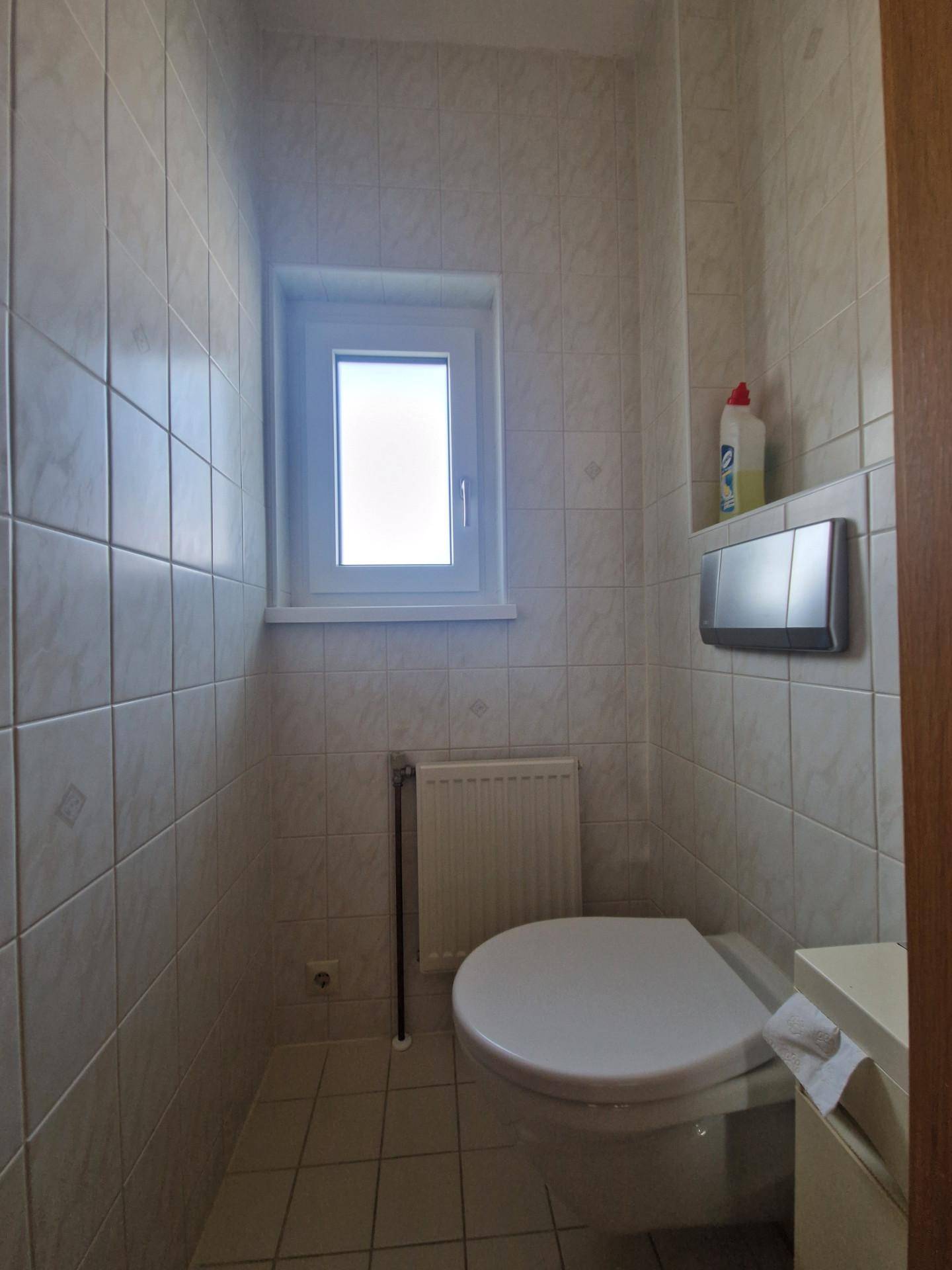 Kleines Gäste-WC mit hellen Fliesen, Fenster und wandhängendem WC.