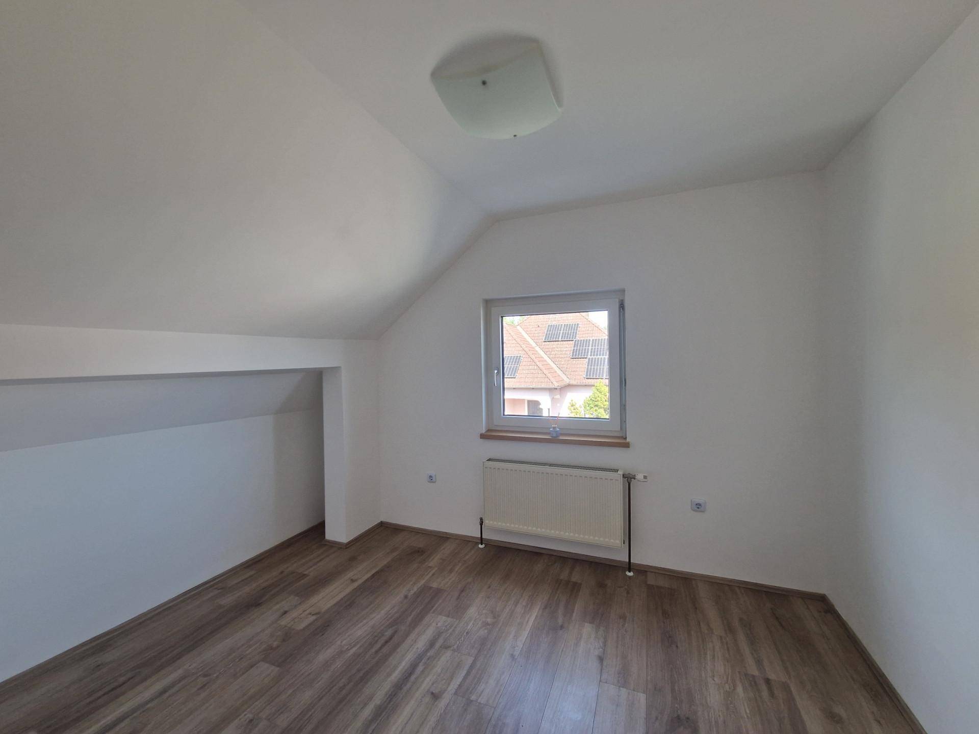 Dachgeschosszimmer mit Laminatboden, schrägen Wänden und Fenster mit Ausblick.