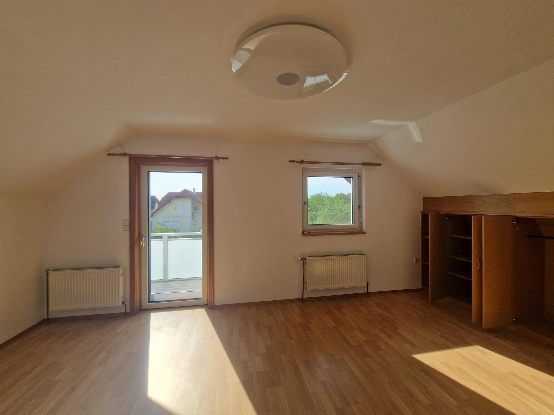 Schlafzimmer im Dachgeschoss mit Laminatboden und direktem Zugang zum Balkon.
