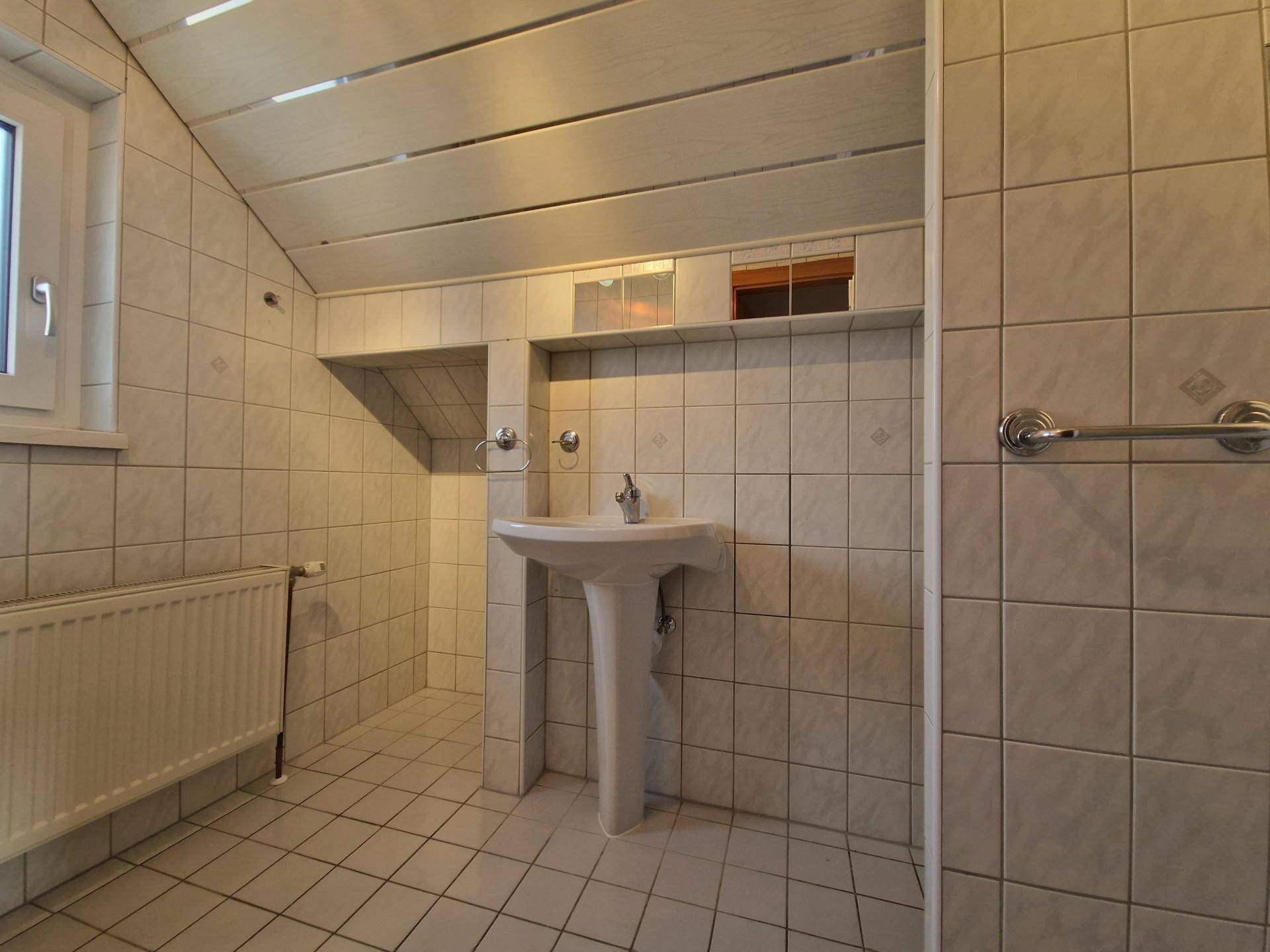 Badezimmer im Dachgeschoss mit Fliesenboden, Waschtisch und Fenster.