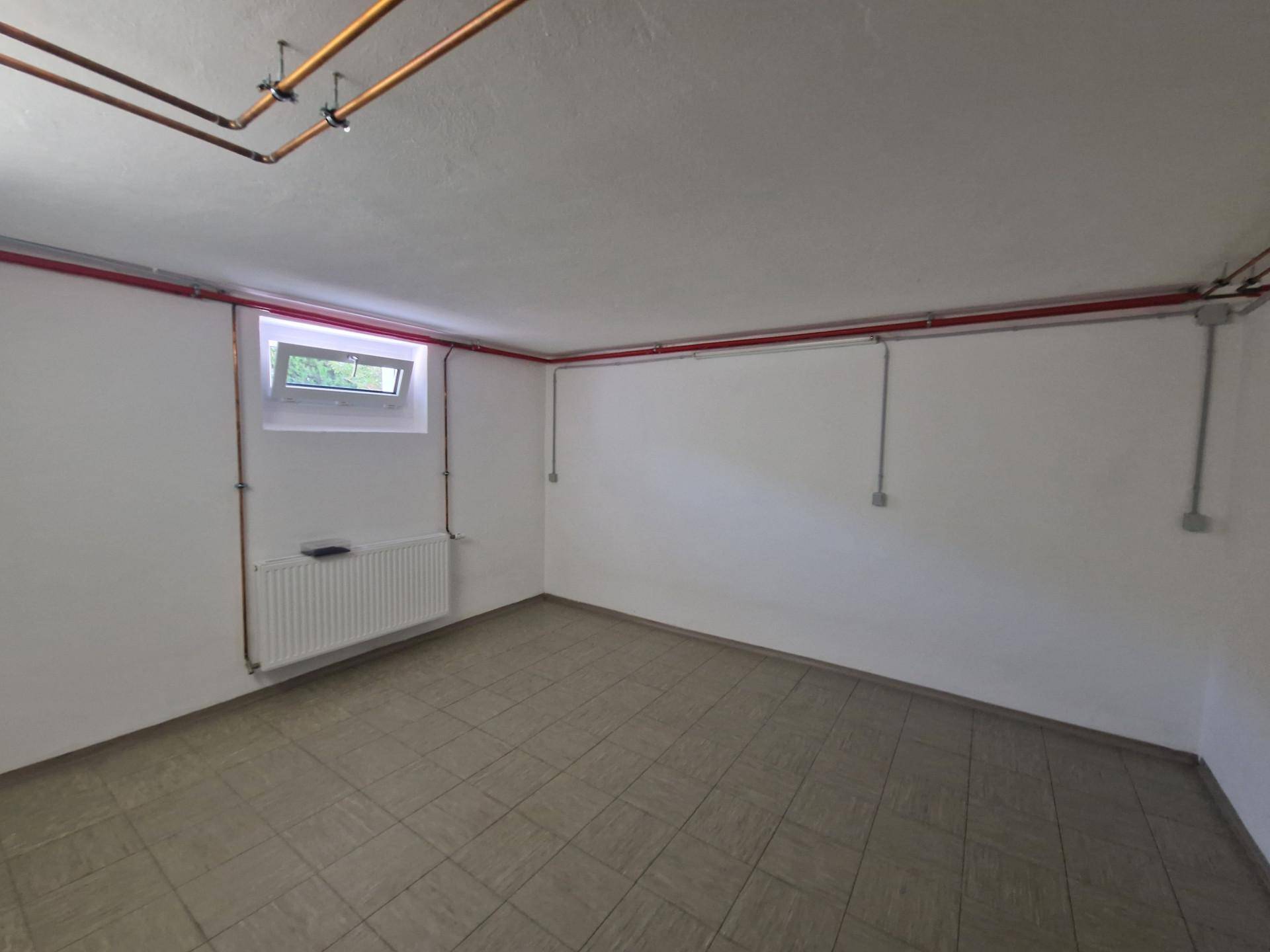 Geräumiger Kellerraum mit Fliesenboden, Heizkörper und kleinem Fenster.