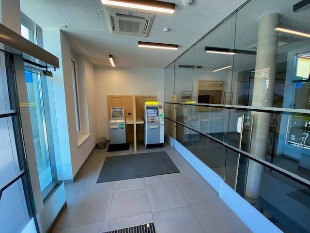 Heller Eingangsbereich einer Bank mit Geldautomaten, moderner Glasabtrennung und Fliesenboden.