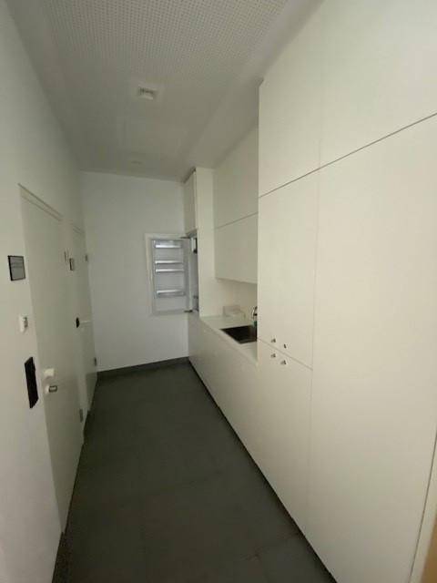 Kleine Küchenzeile mit weißen Schränken, Spüle und integriertem Kühlschrank in einem Flurbereich.