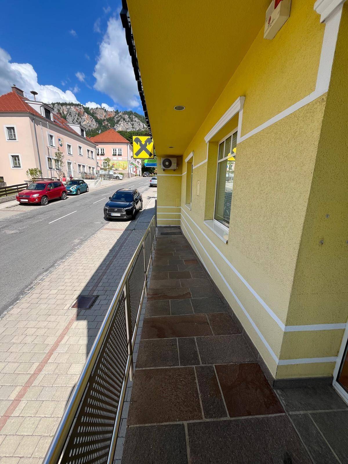 Außenbereich mit barrierefreier Rampe und Steinplattenboden entlang der gelben Gebäudefassade.