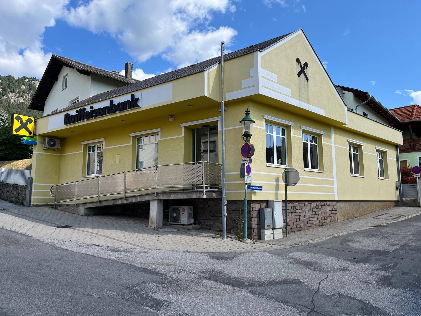 Gelbes Geschäftsgebäude mit Rampe und Raiffeisenbank-Beschriftung unter blauem Himmel.