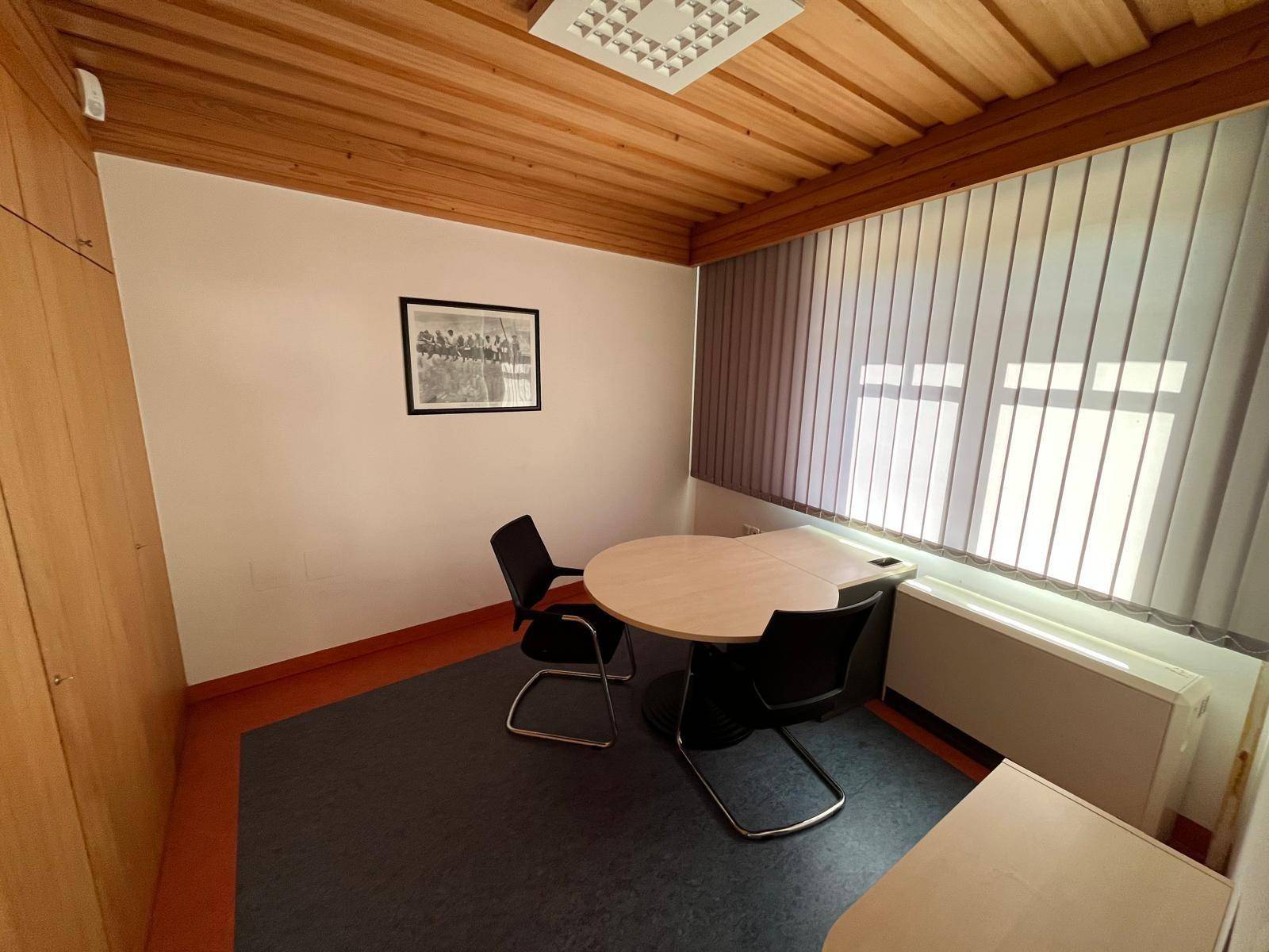 Kleines Büro mit Holzwänden, Holzdecke und einem runden Tisch für Besprechungen.