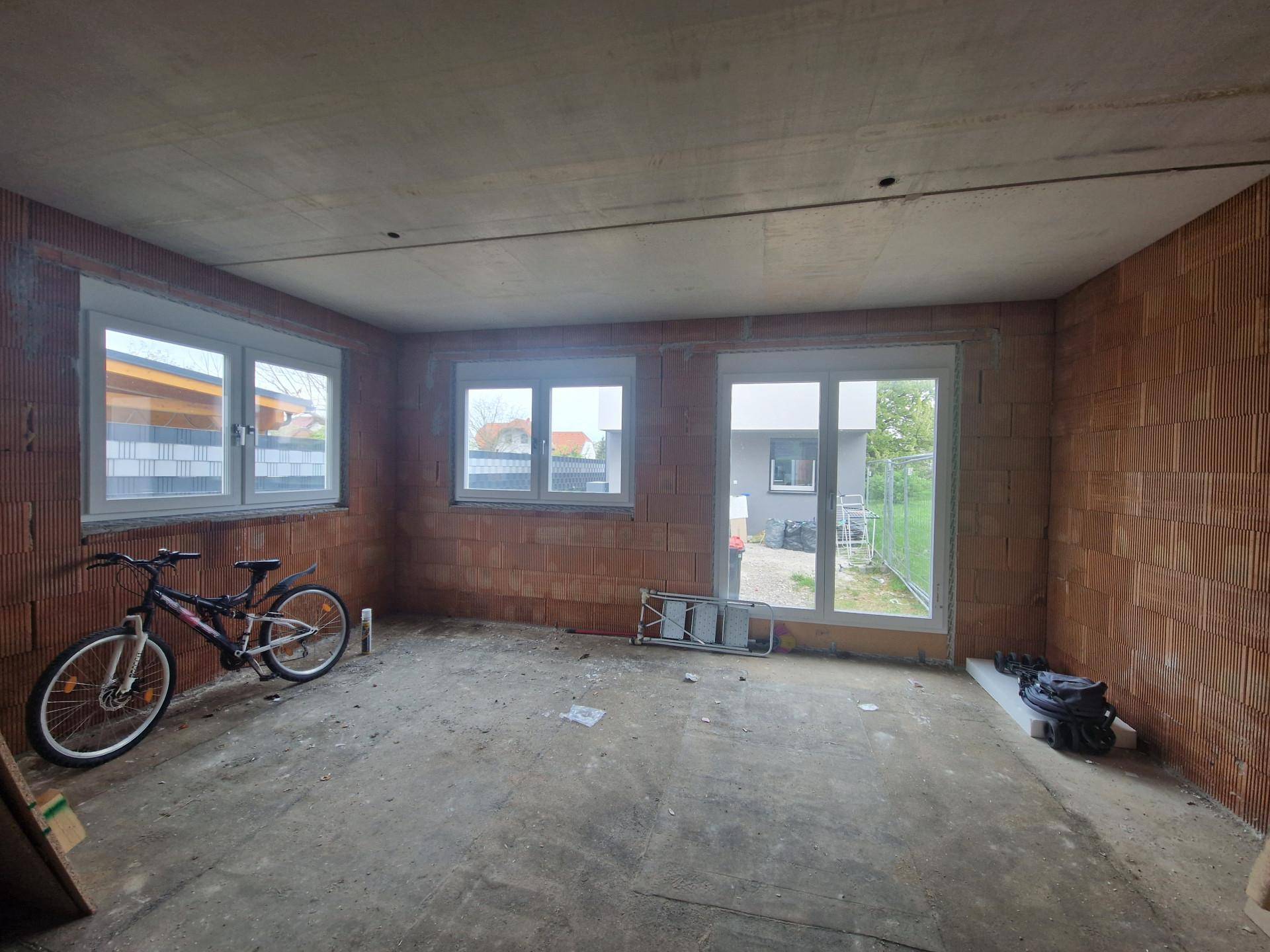 Unfertiger Innenraum mit Ziegelwänden, Betonboden und großen Fenstern, bereit für den Ausbau.