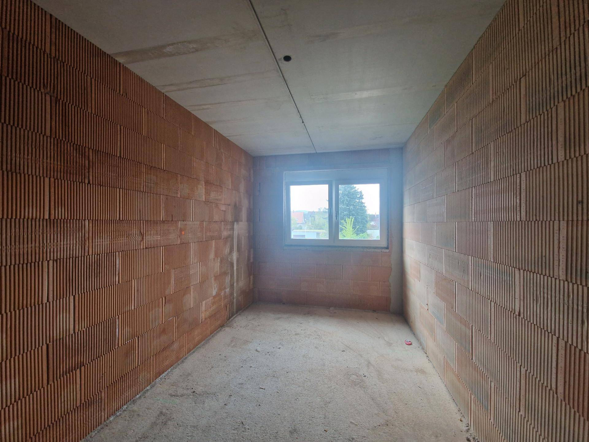Unfertiger Raum mit Ziegelwänden, Betonboden und einem Fenster, das Tageslicht hereinlässt.