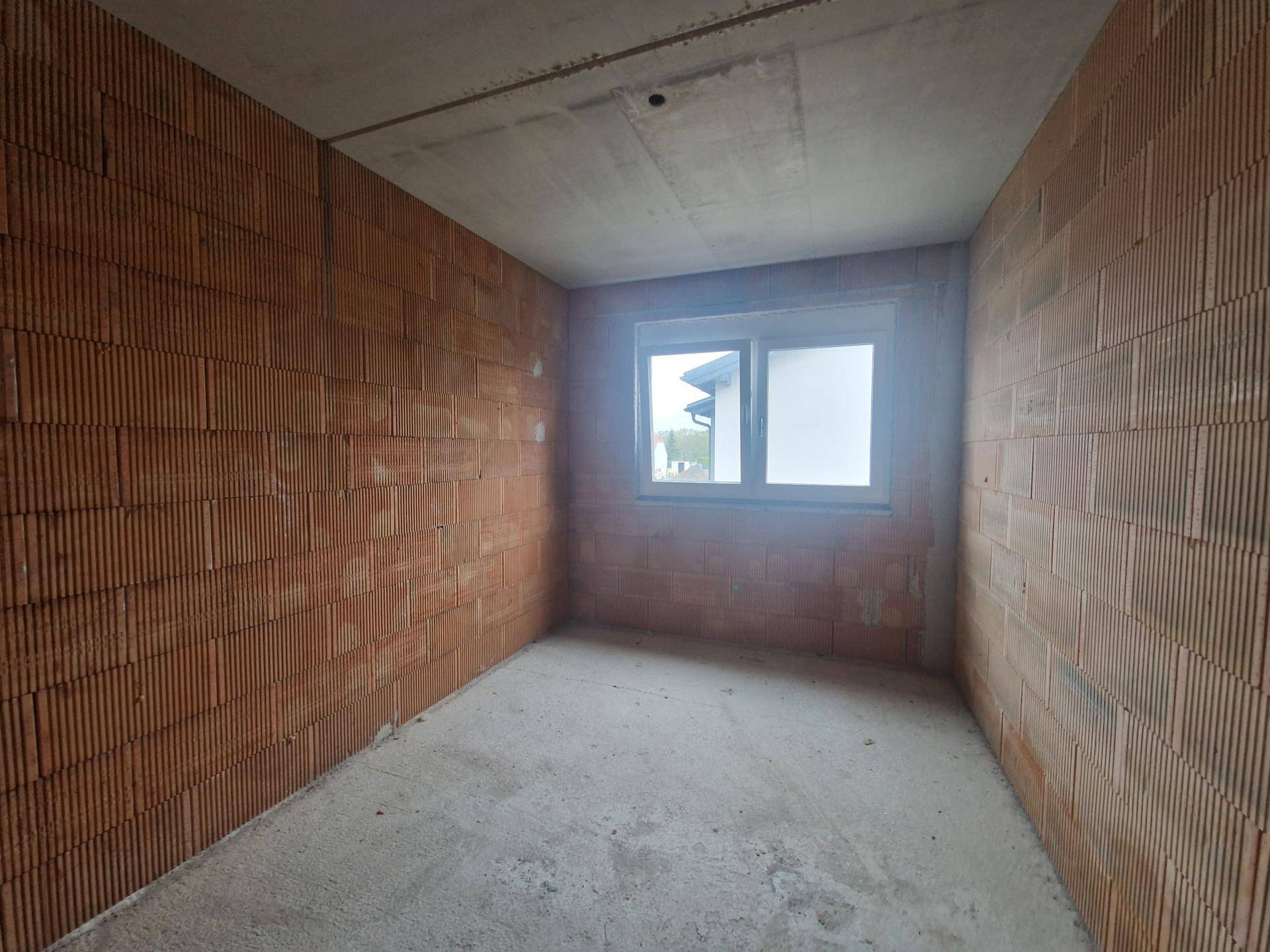 Unfertiger Raum mit Ziegelwänden und Betonboden, der auf den Innenausbau wartet.
