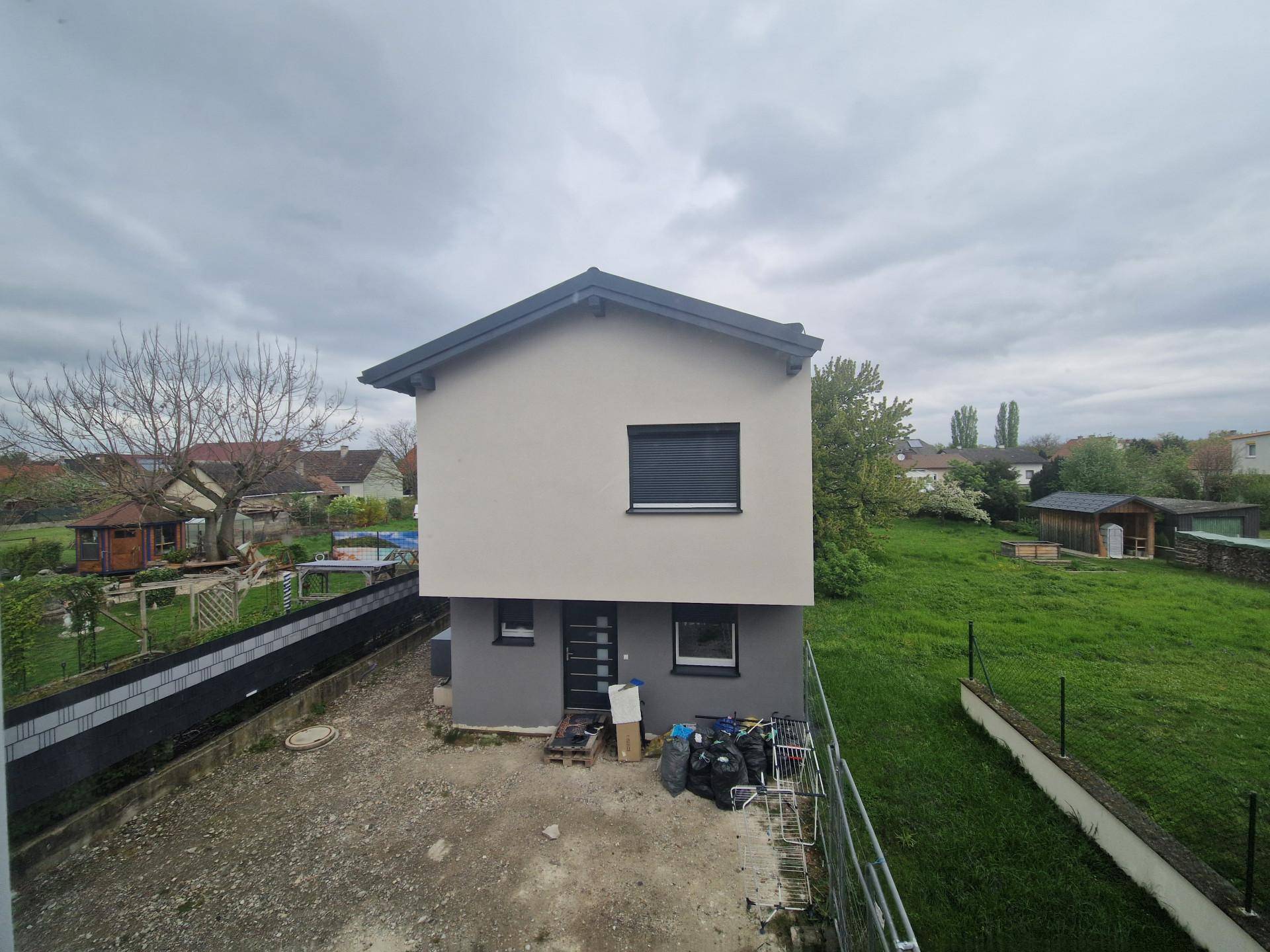 Neues Einfamilienhaus mit moderner Fassade, Flachdach und Rollläden, umgeben von Grünflächen.