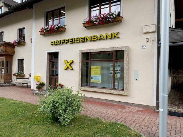 Nahaufnahme des Eingangs der Raiffeisenbank mit Blumenkästen an den Fenstern und dem markanten Banklogo.