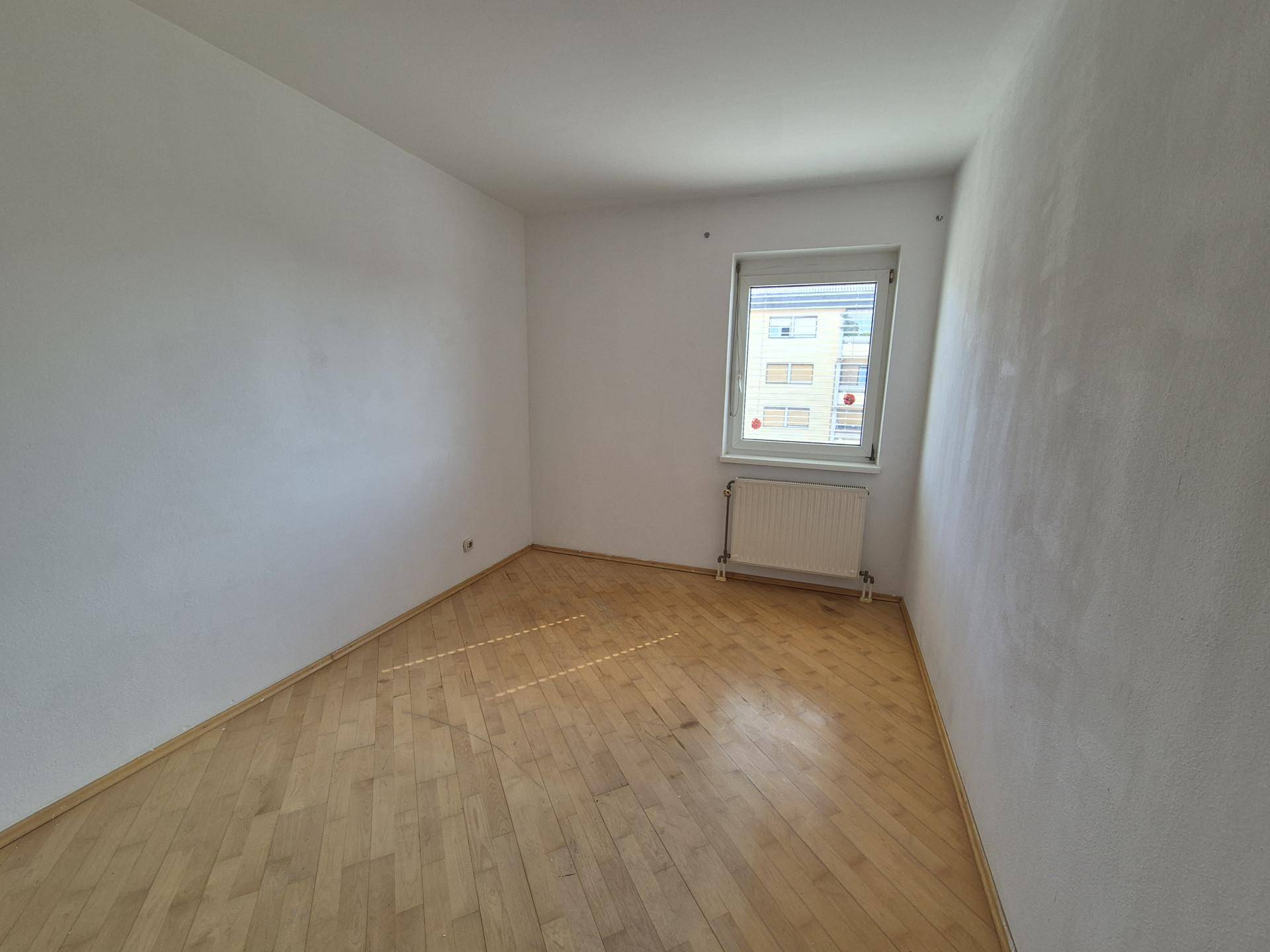 Leeres Zimmer mit Holzboden und Fenster, ideal als Schlaf- oder Arbeitszimmer nutzbar.