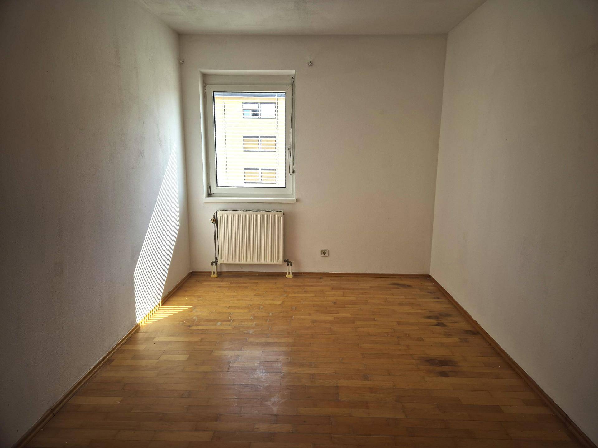 Helles, leeres Zimmer mit Holzboden und Fenster, bereit zur individuellen Gestaltung.
