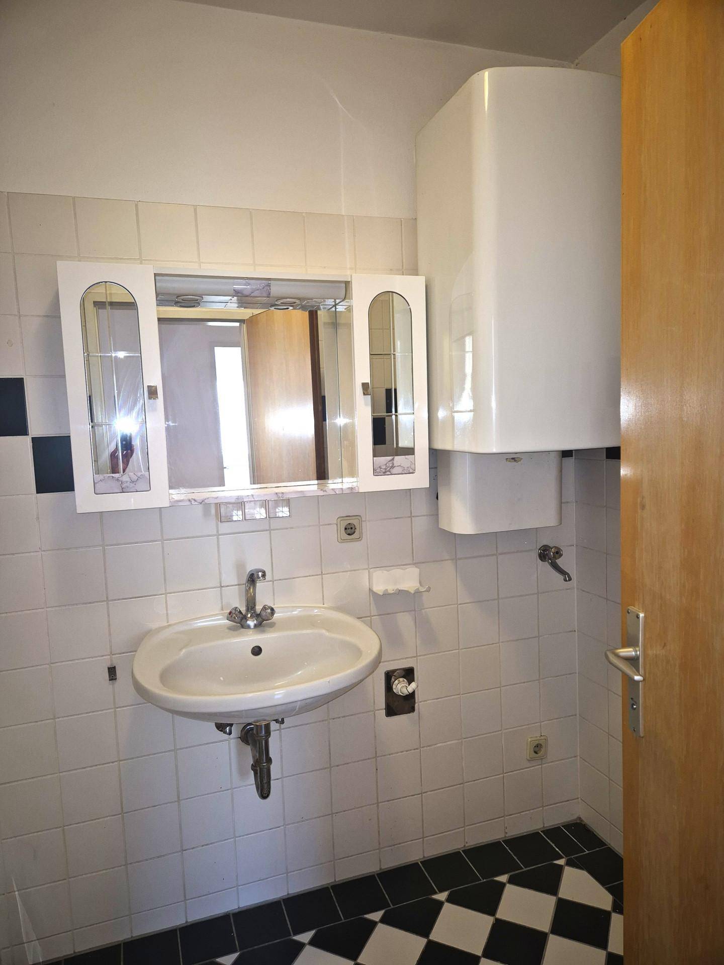 Badezimmer mit Waschbecken, Spiegelschrank und Warmwasserboiler an der Wand.