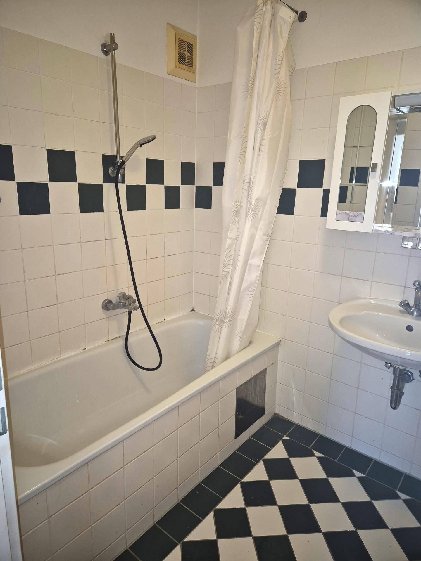 Badezimmer mit Badewanne, Duschvorhang und markanten schwarz-weißen Fliesen.
