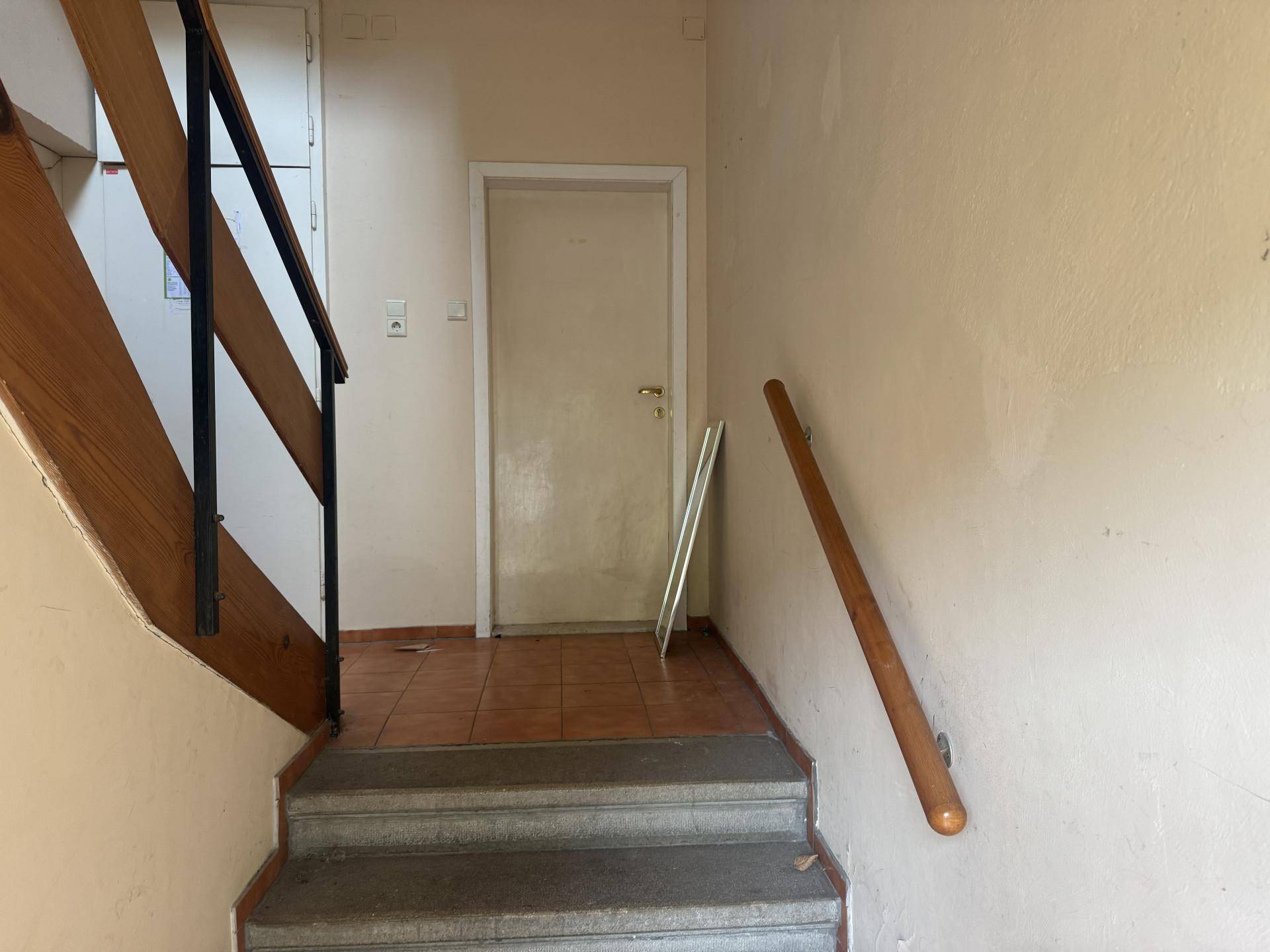 Treppenhaus mit Steinstufen, Holzgeländer und gefliestem Podest, das in die obere Etage führt.