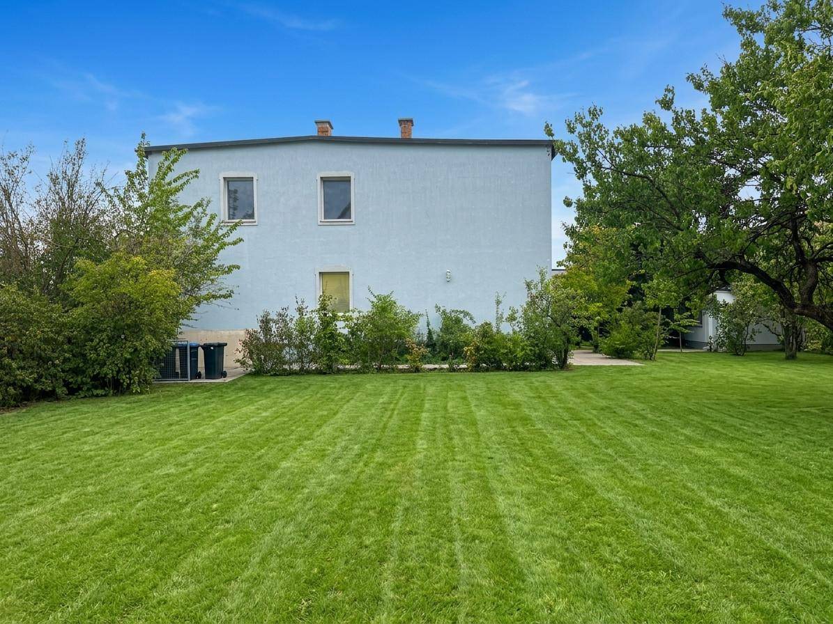 Rückansicht des Hauses mit weitläufigem, grünem Rasen und Sträuchern im Gartenbereich.