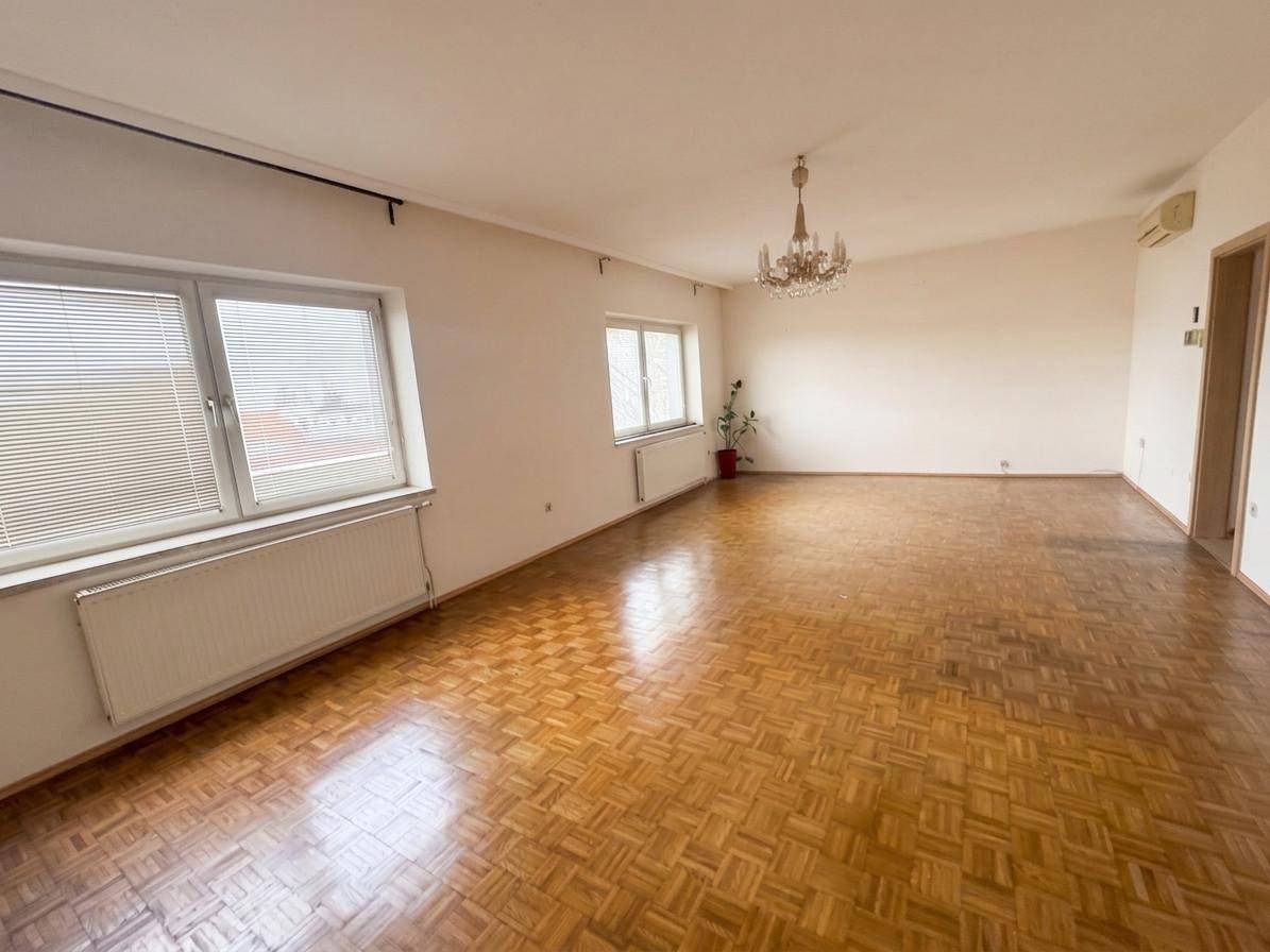 Geräumiges, leeres Wohnzimmer mit klassischem Parkettboden, weißen Wänden und Kronleuchter.