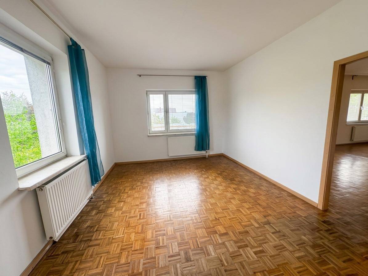 Leeres Schlafzimmer mit Parkettboden, weißen Wänden und blauen Vorhängen an den Fenstern.