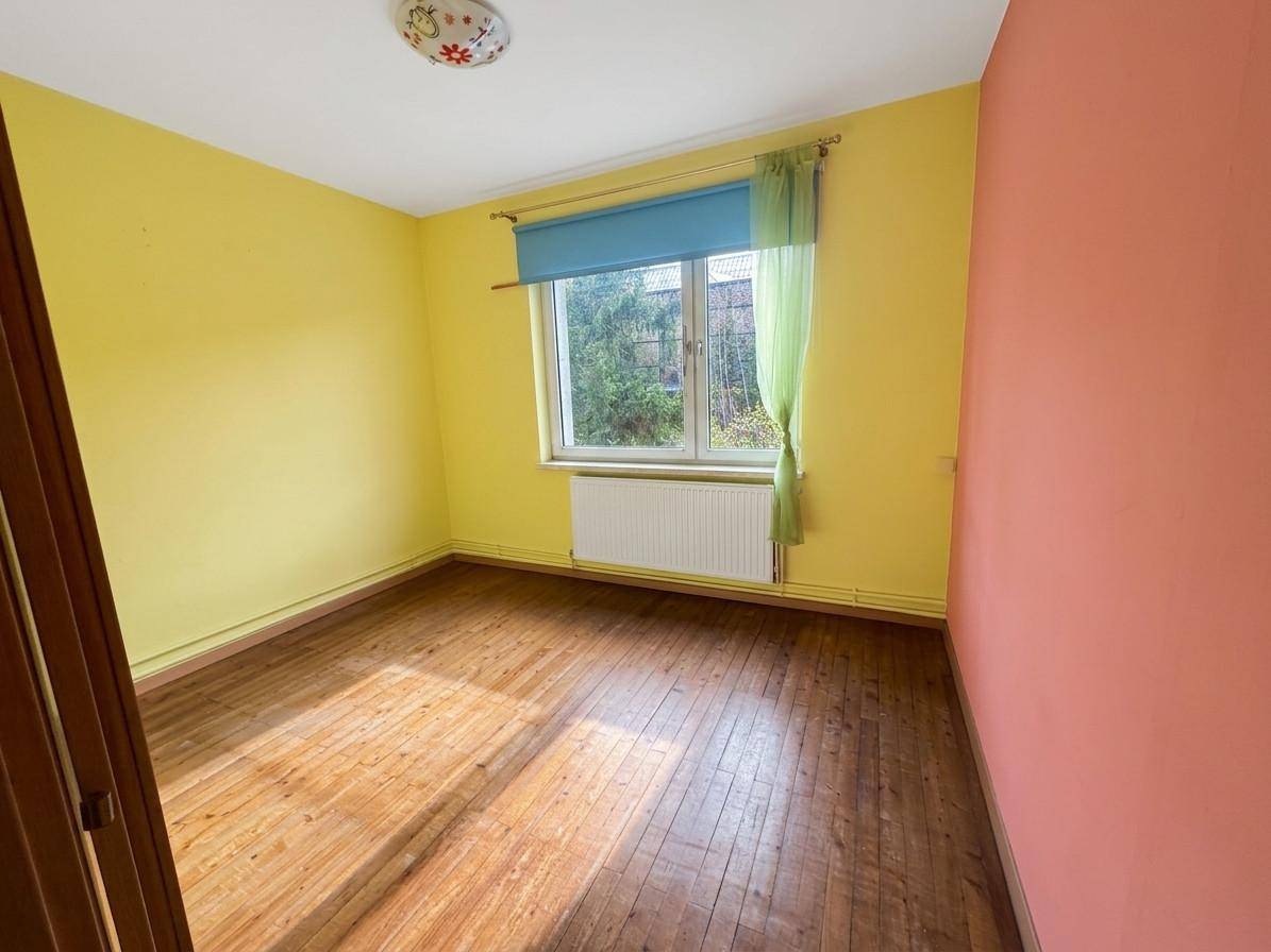 Buntes Zimmer mit Holzdielenboden, gelben und rosa Wänden sowie einem Fenster mit Vorhängen.