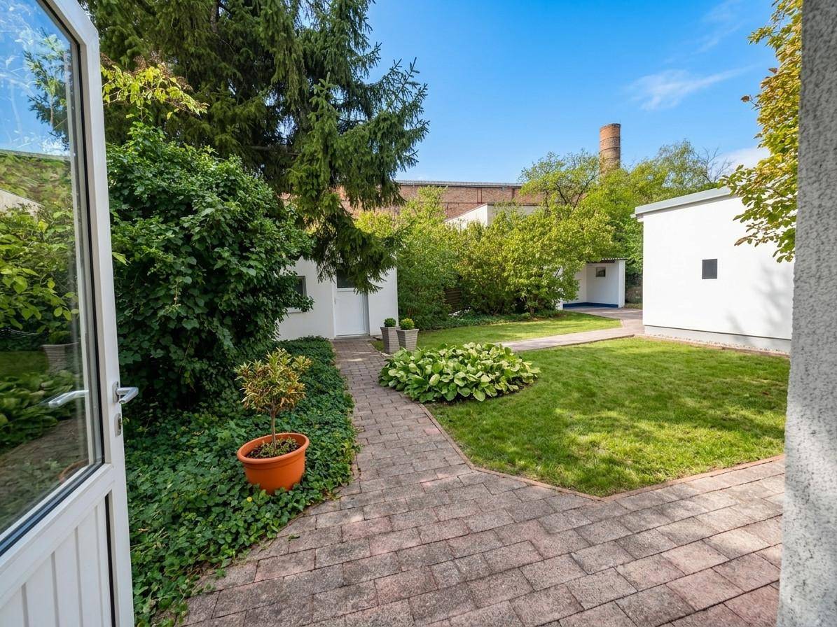 Gepflasterter Terrassenbereich führt zu einem gepflegten Garten mit Rasen und Nebengebäuden.