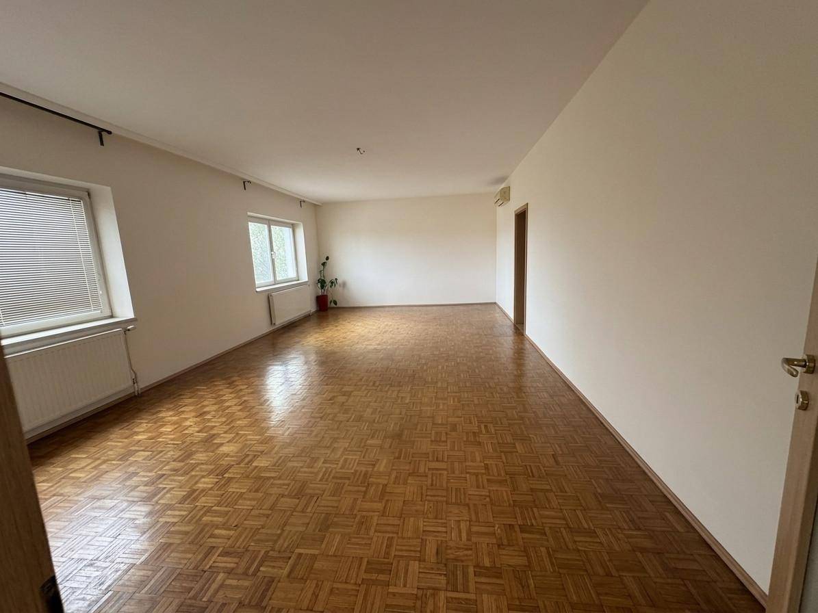 Weitläufiges, leeres Wohnzimmer mit glänzendem Parkettboden und großen Fenstern für viel Licht.