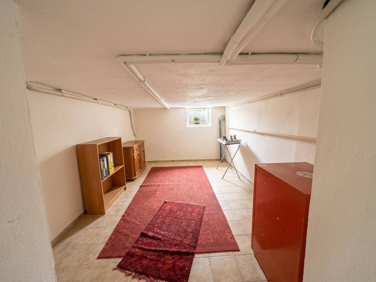 Kellerraum mit Fliesenboden, Regalen und rotem Schrank, ideal als Abstell- oder Hobbyraum.
