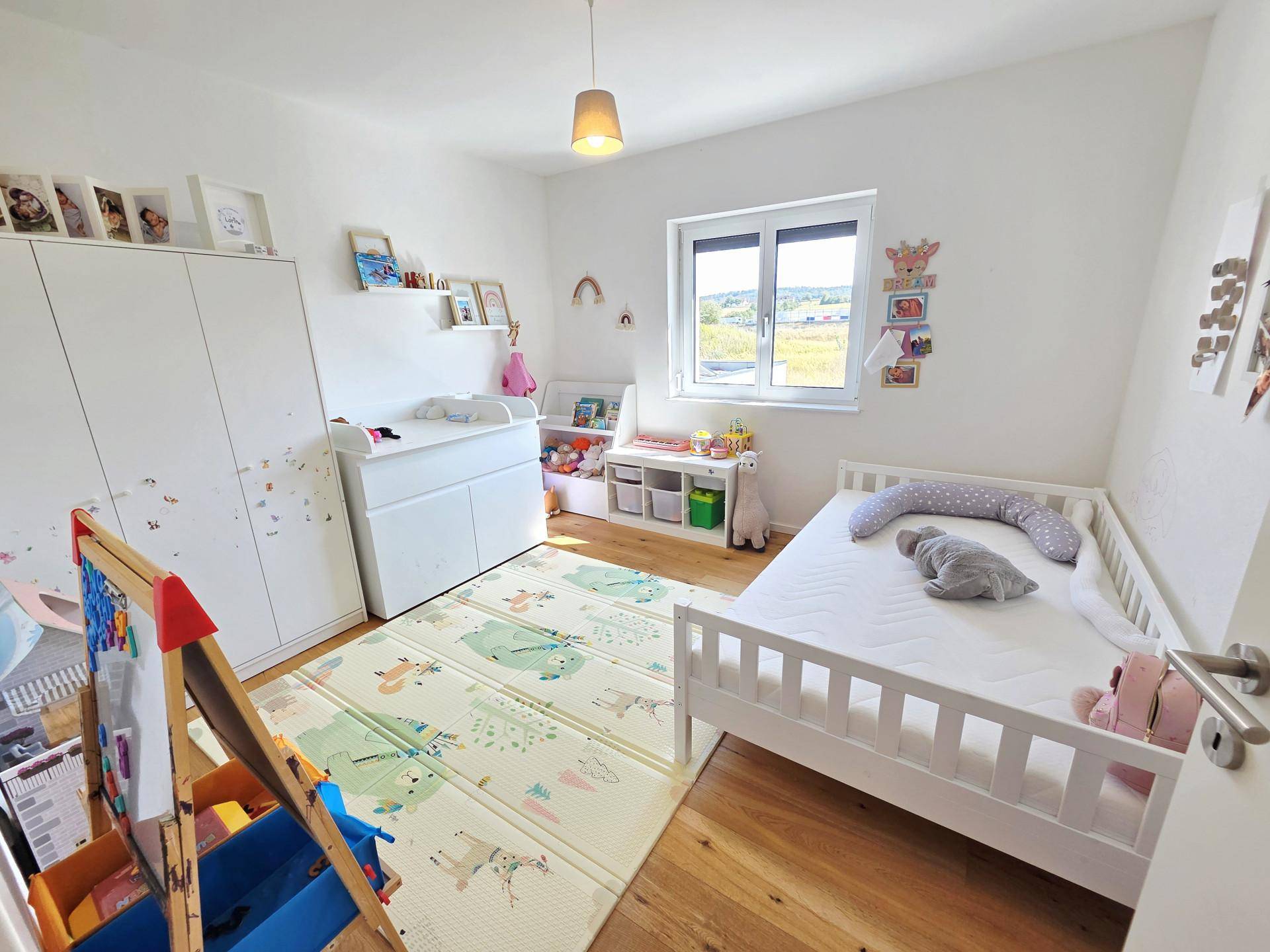 Helles Kinderzimmer mit Holzboden, Spielmatte und weißen Möbeln, freundlich eingerichtet.