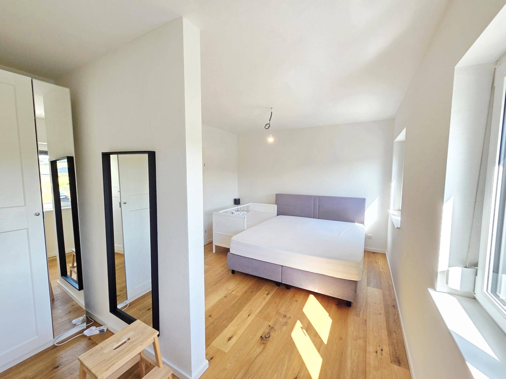 Schlafzimmer mit Holzboden, großem Bett und weißen Kleiderschränken, hell und geräumig.