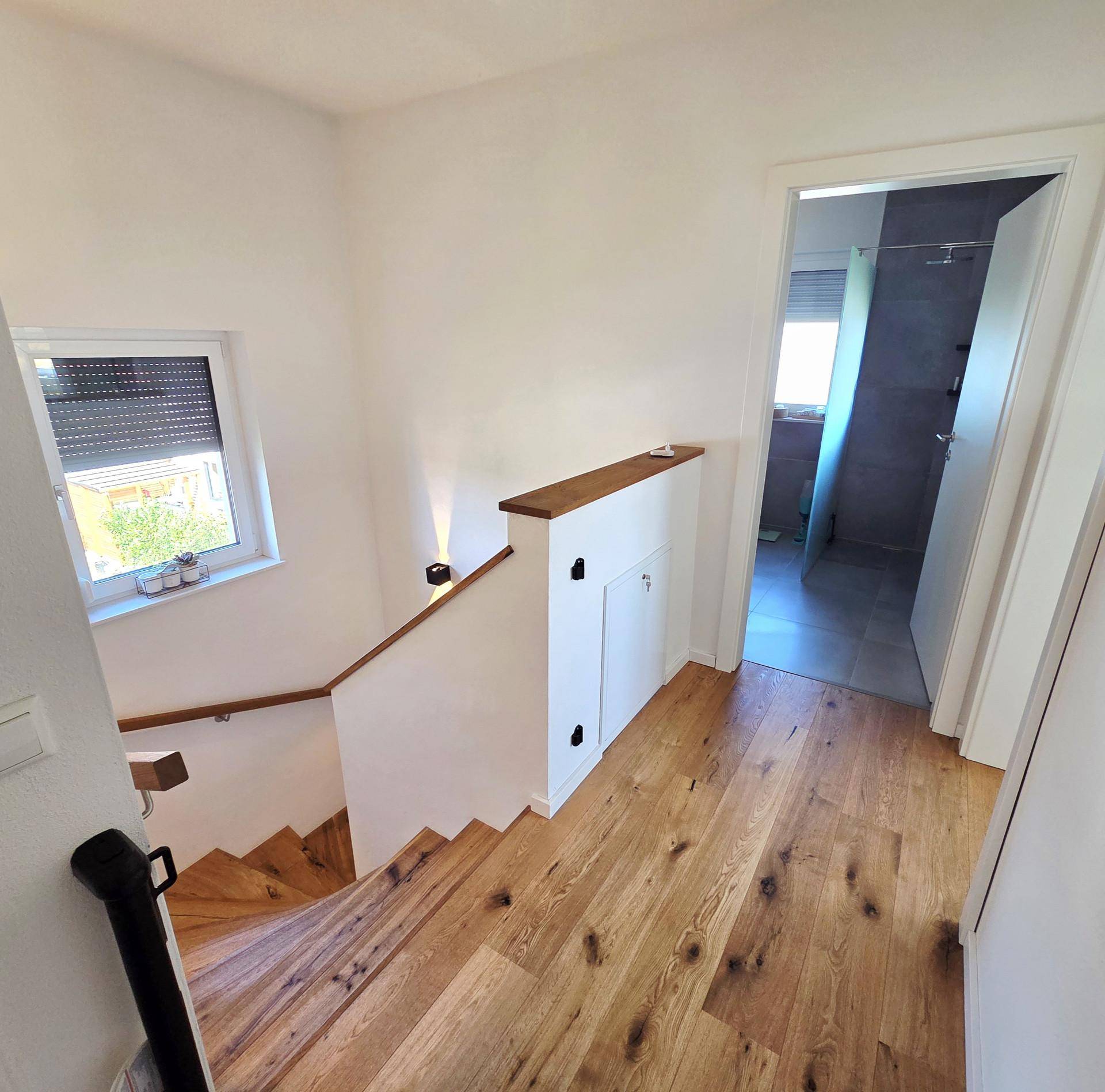 Heller Flur mit Holztreppe und Fenster, das natürliches Licht hereinlässt.