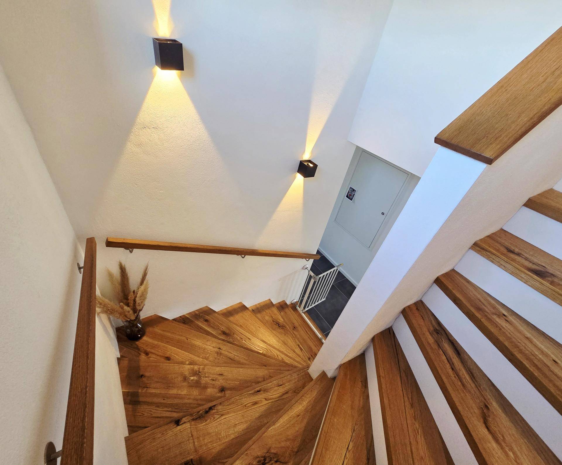 Elegante Holztreppe mit modernen Wandleuchten, die den Aufgang beleuchten.