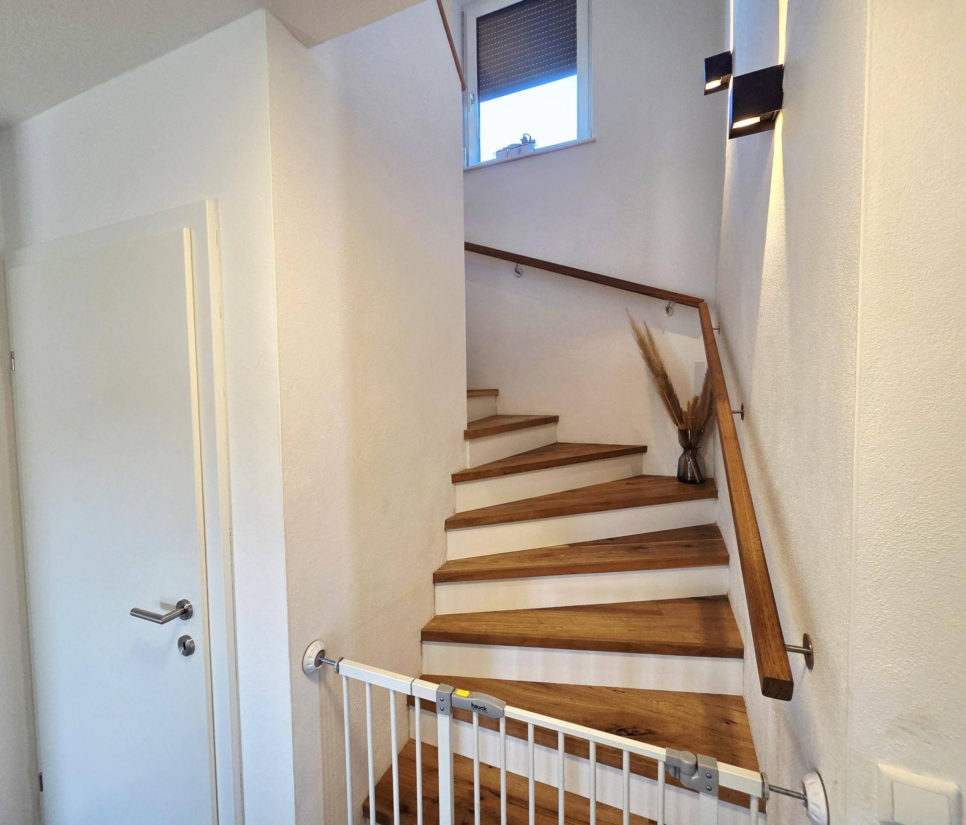 Holztreppe mit Kinderschutzgitter und natürlichem Lichteinfall durch ein Fenster.