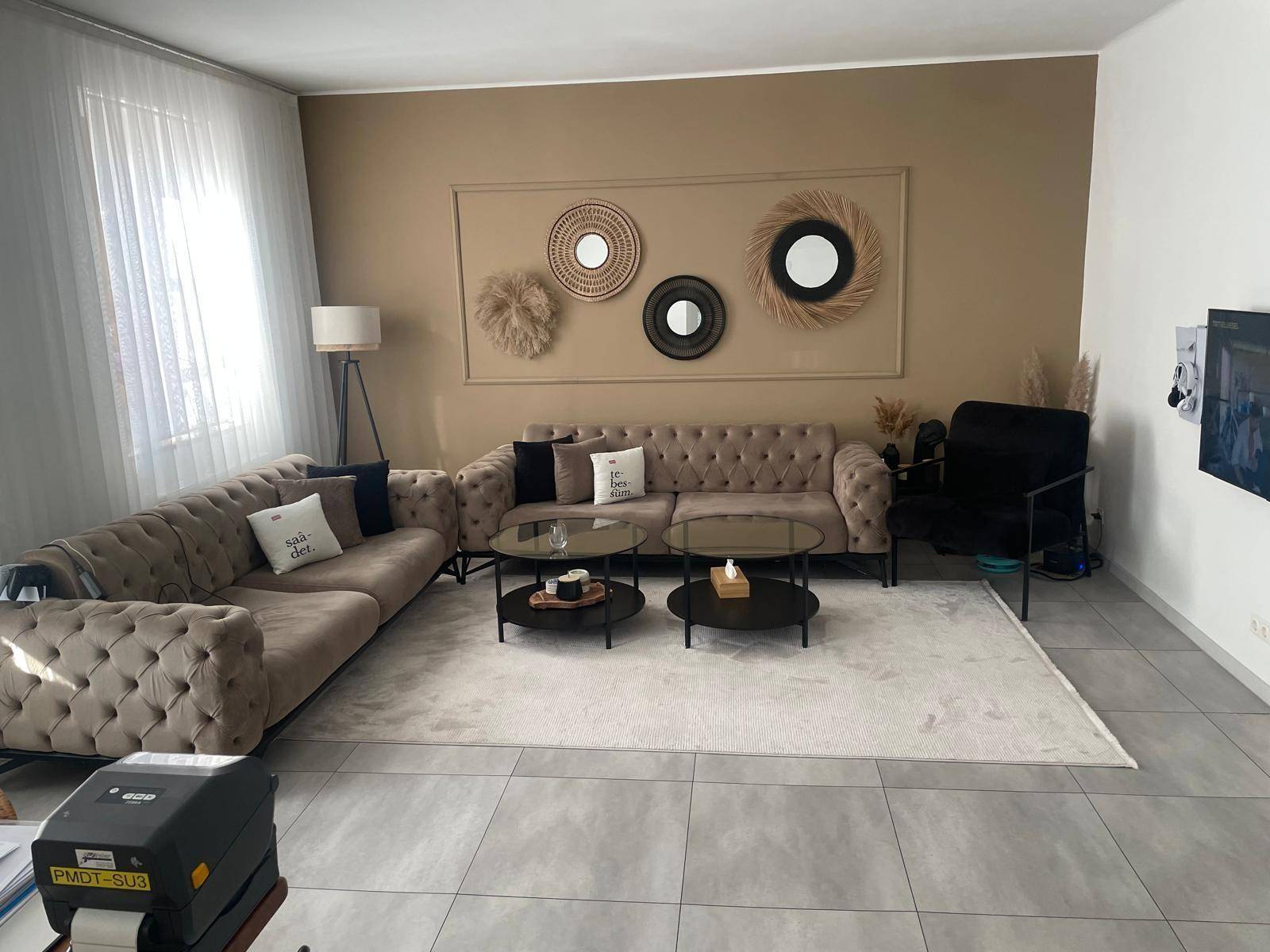 Geräumiges Wohnzimmer mit beigen Sofas, modernen Spiegeln und hellem Fliesenboden.