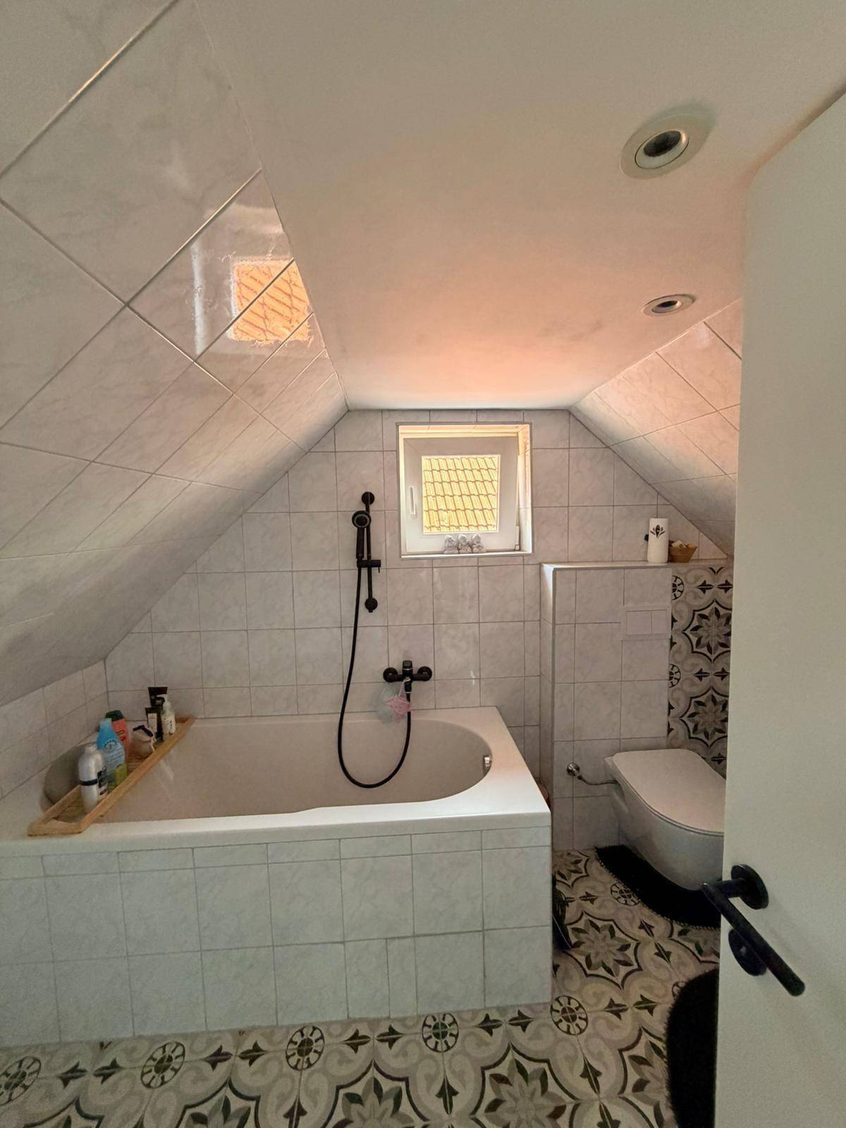 Badezimmer im Dachgeschoss mit Badewanne, WC und gemusterten Fliesen.