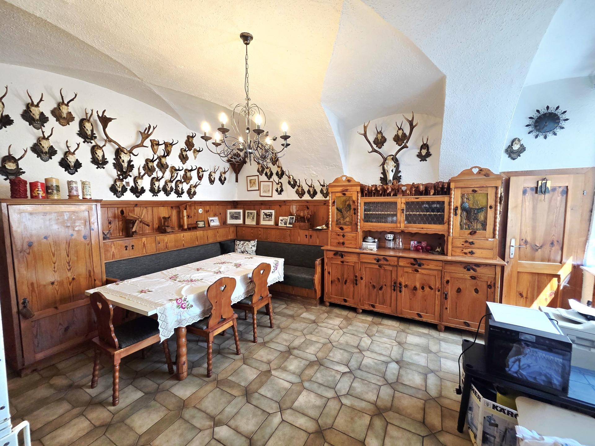Traditioneller Essbereich mit Holztisch, Eckbank, Geweihsammlung und einer markanten gewölbten Decke.
