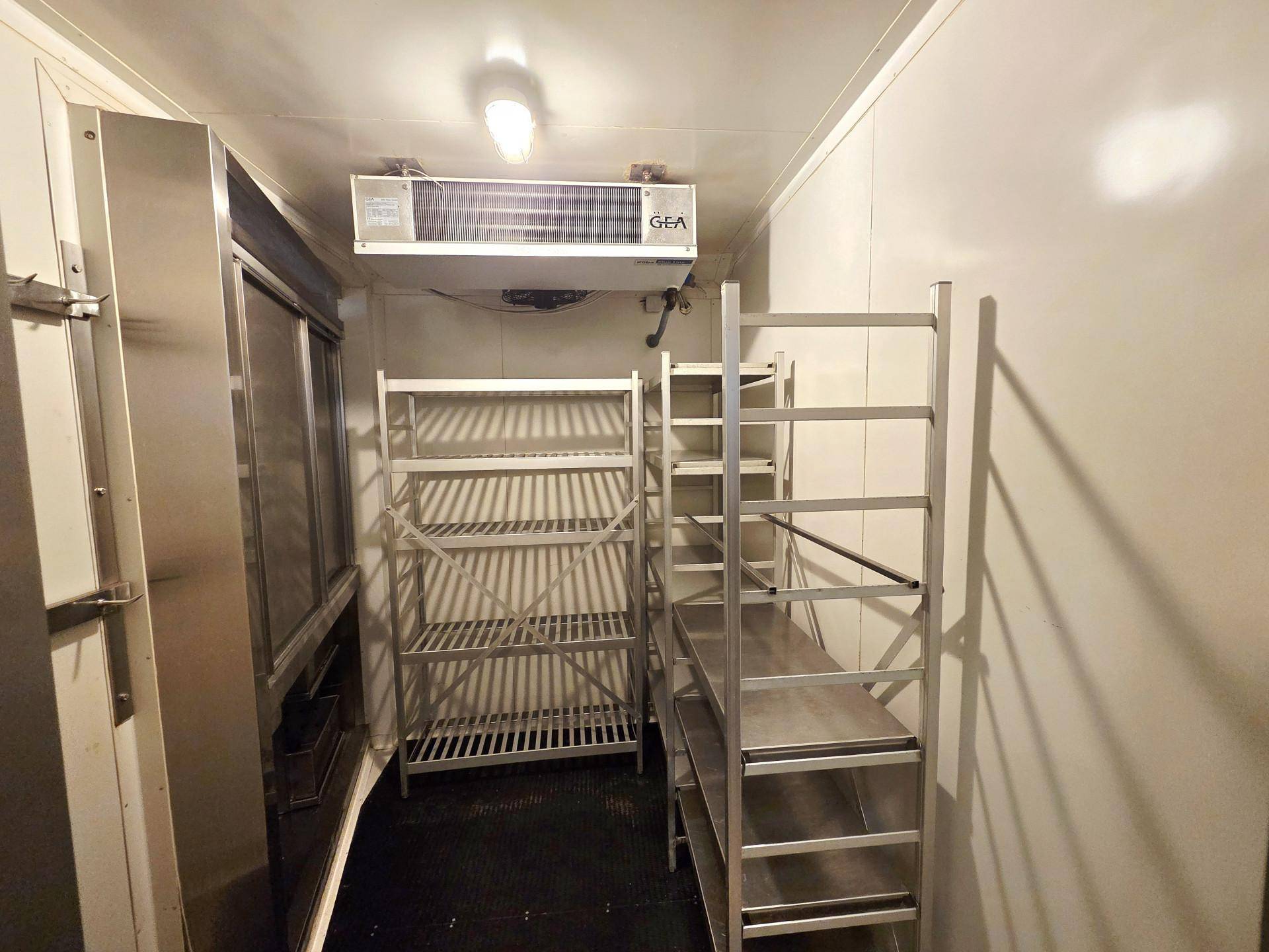 Innenansicht eines Kühlraums mit Metallregalen und industrieller Kühlanlage an der Decke für Lagerzwecke.