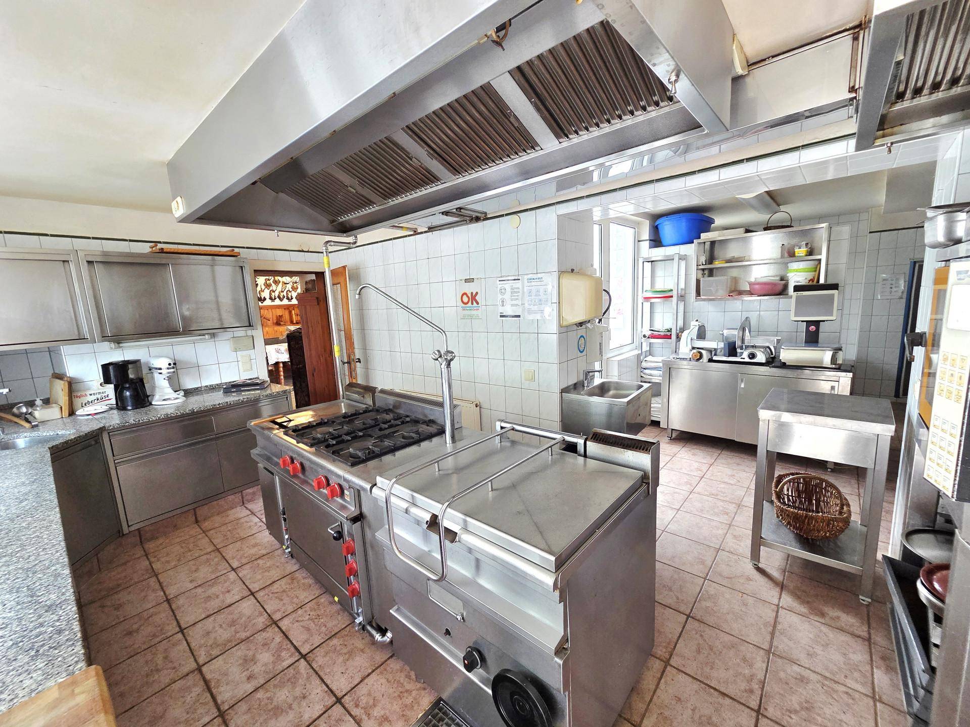 Geräumige Gewerbeküche mit umfangreicher Edelstahlausstattung, Gasherd und Fliesenboden, bereit zum Kochen.