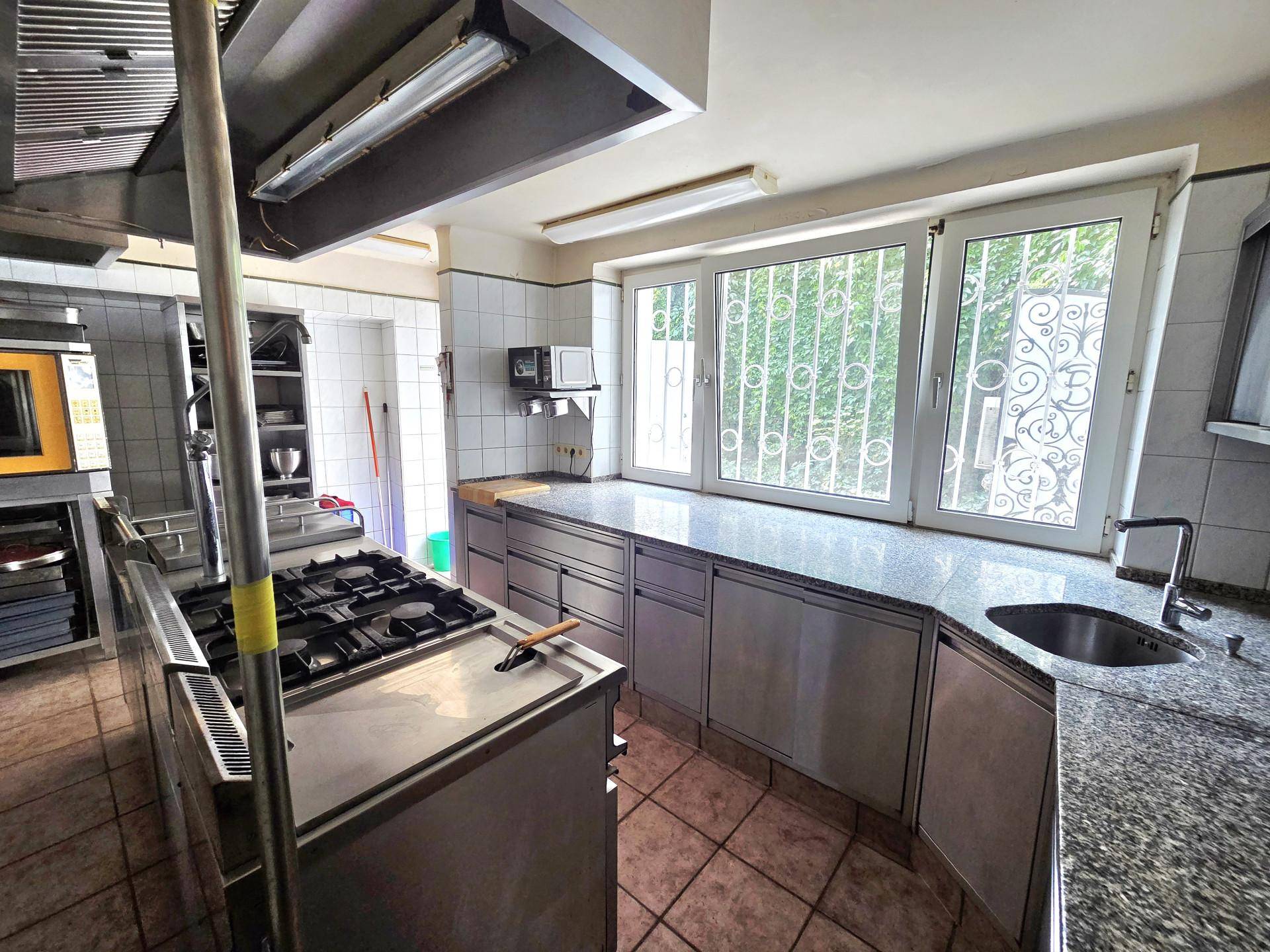 Professionelle Küche mit Edelstahlmöbeln, Gasherd und großem Fenster mit Gitter, ideal für Gastronomie.