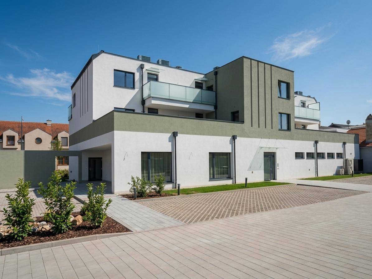 Rückansicht eines modernen Gebäudes mit Parkplätzen und begrünten Außenbereichen unter klarem Himmel.