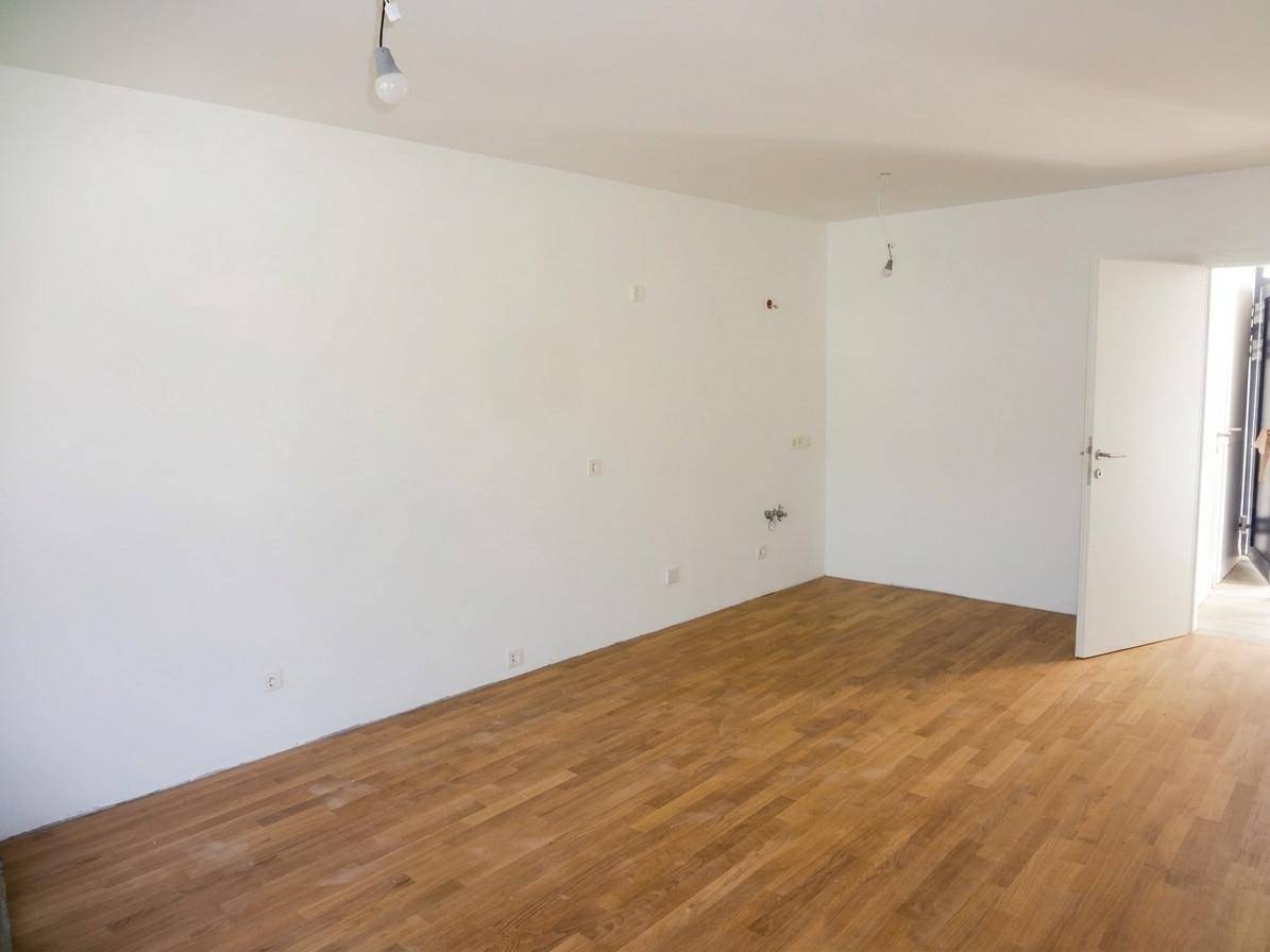 Leerer Raum mit Holzboden und weißen Wänden, vorbereitet für die Installation einer Küche.
