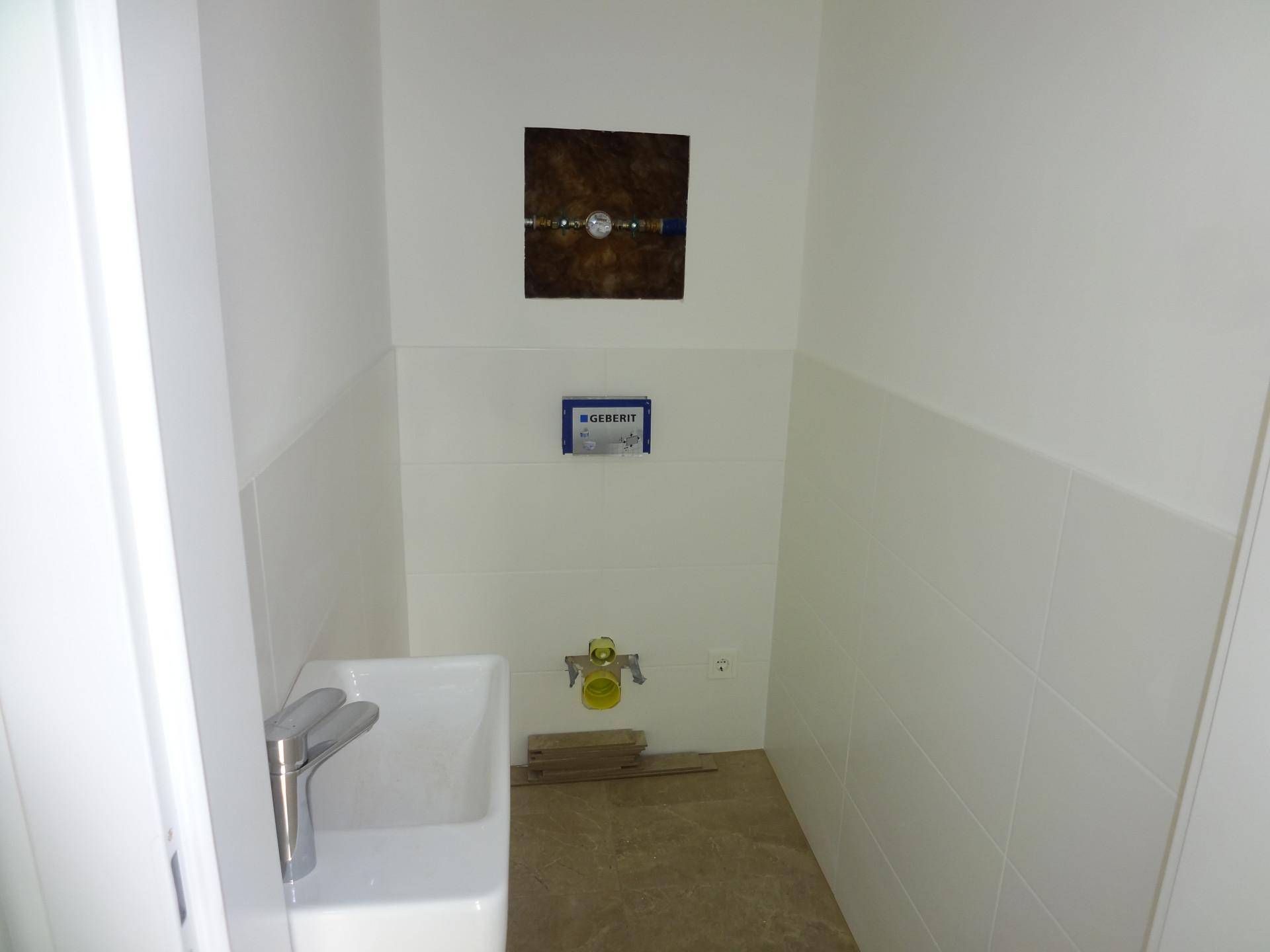 Unmöbliertes Gäste-WC mit Waschbecken und vorbereiteter Toiletteninstallation.