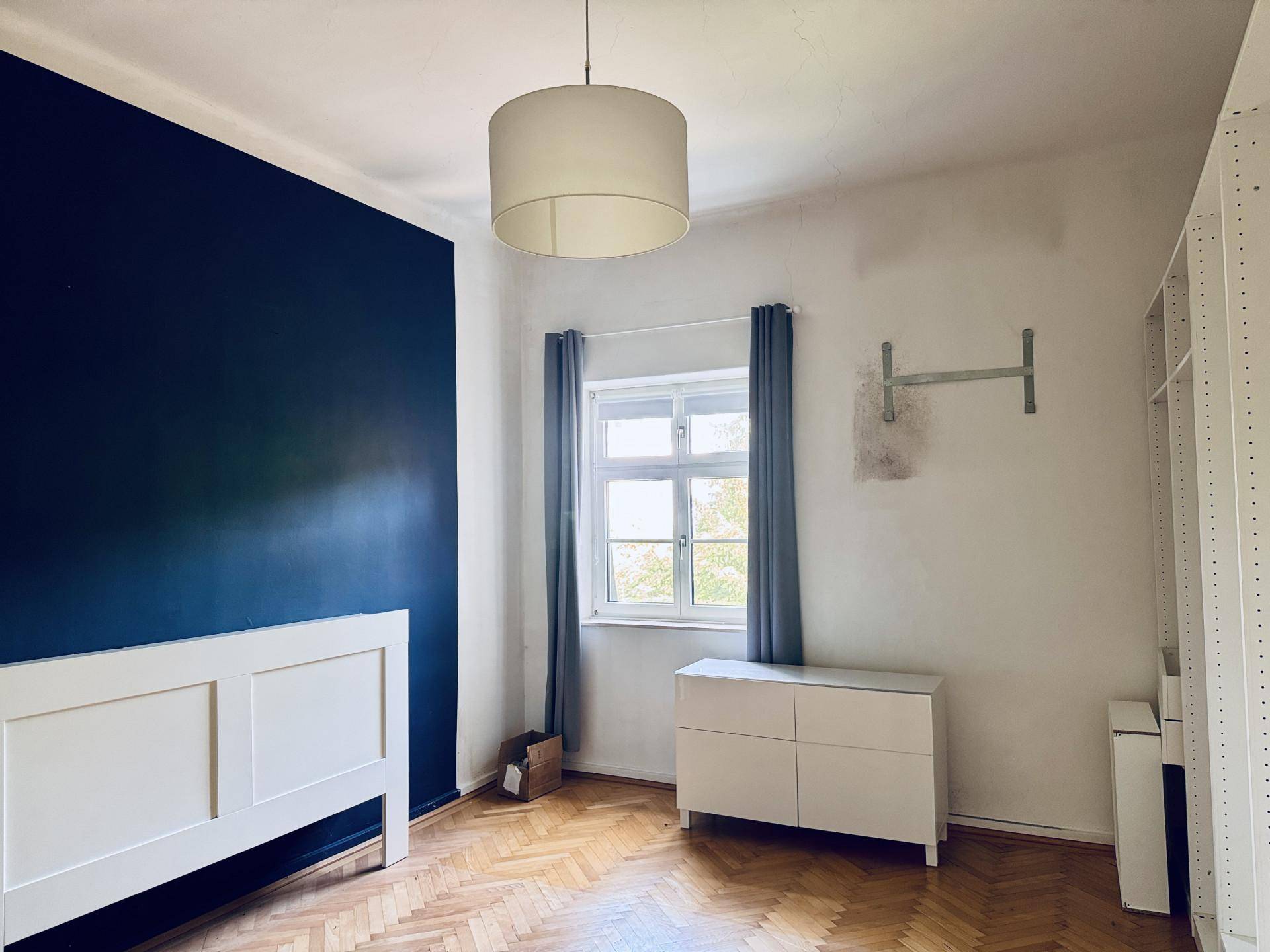 Schlafzimmer mit dunkelblauer Akzentwand, weißem Bettrahmen und klassischem Fischgrätparkettboden.