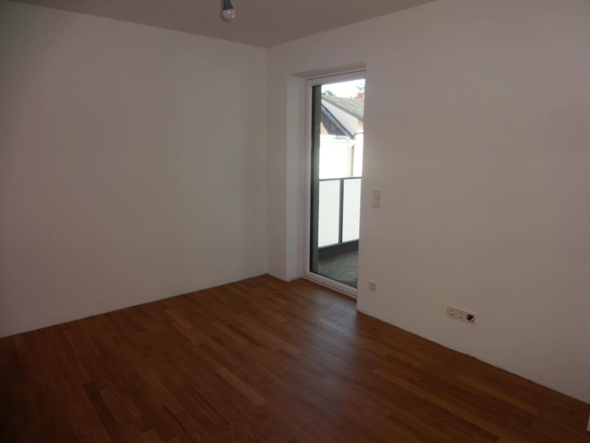 Unmöbliertes Zimmer mit Holzboden und Zugang zu einem kleinen Balkon.