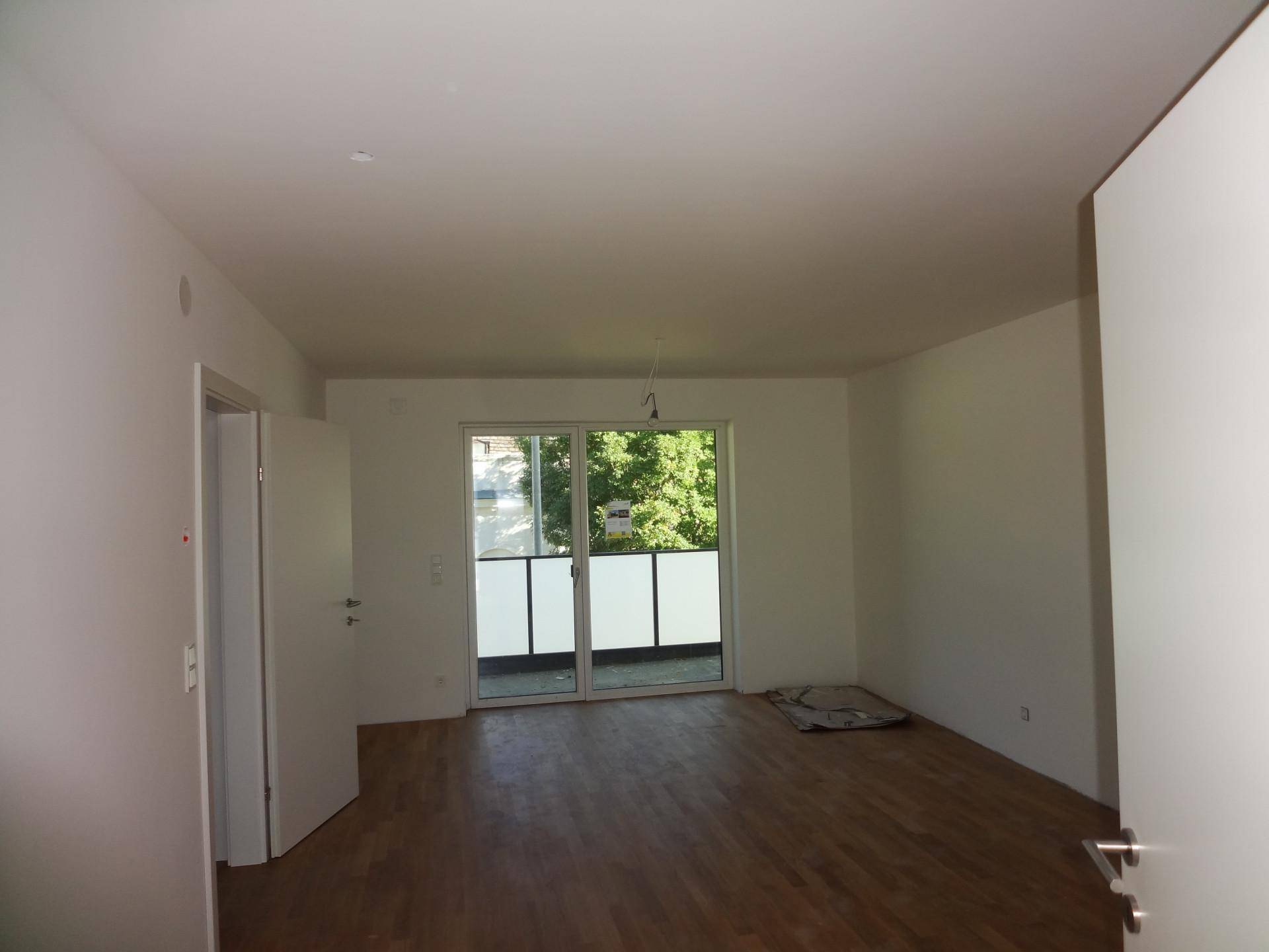 Heller, unmöblierter Raum mit Holzboden und Zugang zu einem Balkon.