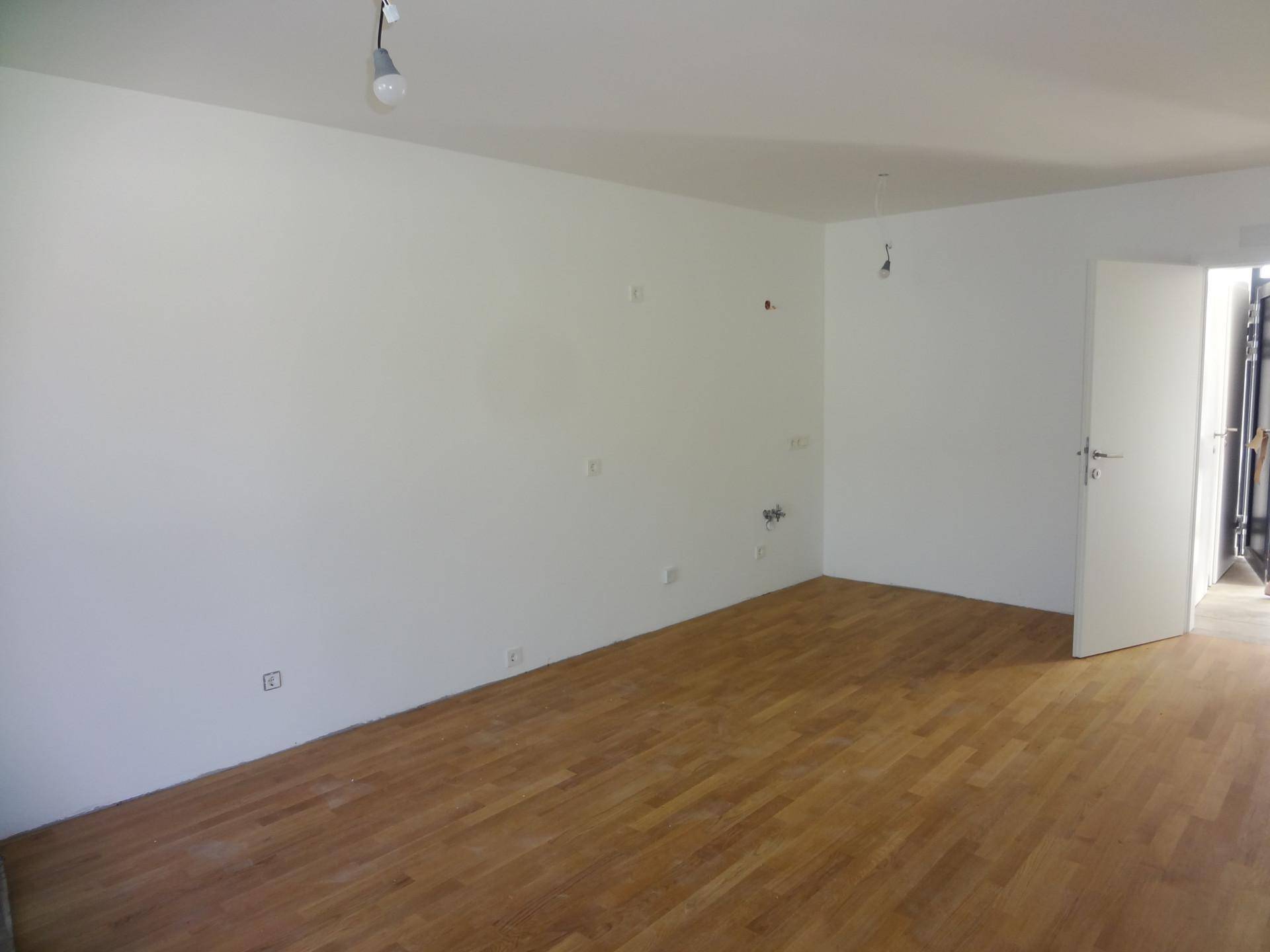 Leerer Küchenbereich mit Holzboden und vorbereiteten Anschlüssen für eine Einbauküche.