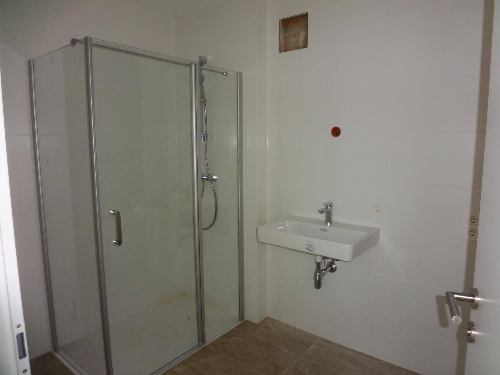 Unmöbliertes Badezimmer mit Duschkabine, Waschbecken und hellen Fliesen.
